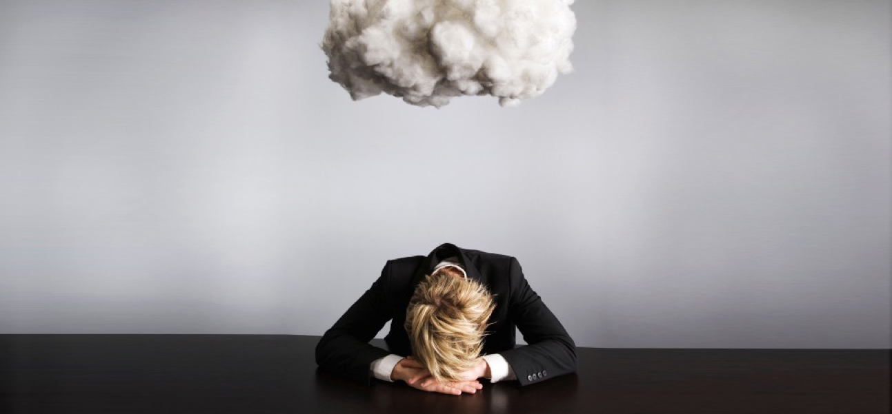 A person in a business suit sitting at a desk with head resting on their hands, and a large cloud of smoke or steam above their head.