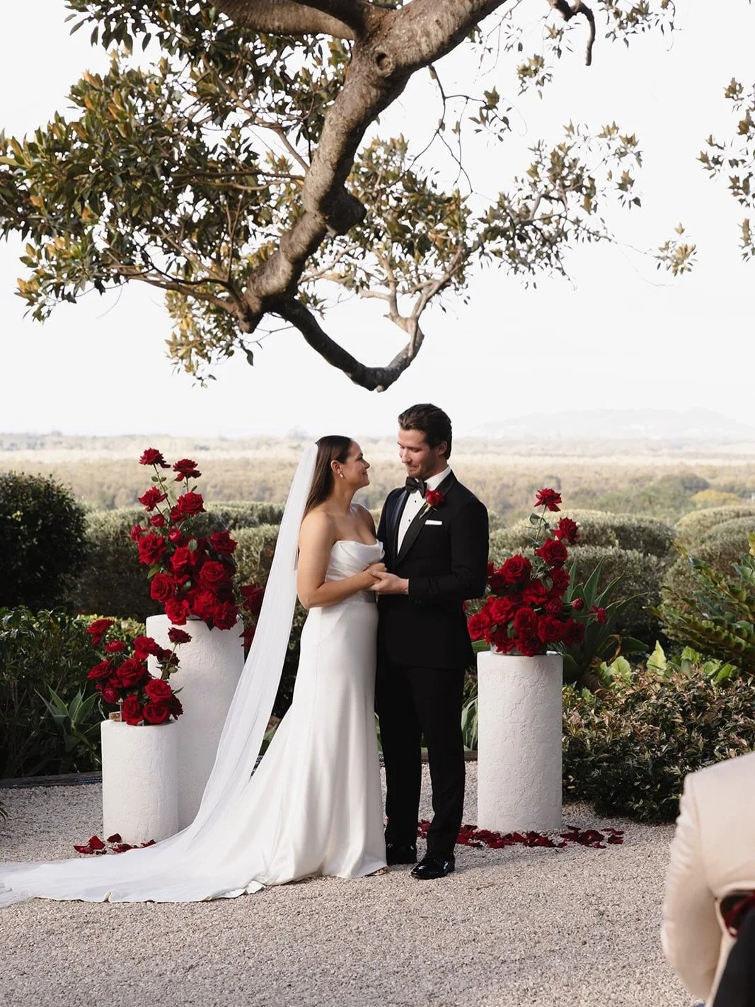 Madie and Jay&rsquo;s ceremony was a masterclass in modern romance. The architectural pillars of deep red roses provided the perfect bold contrast against the lush greenery, creating a space that felt both intimate and grand. Red ribbons tied on the 
