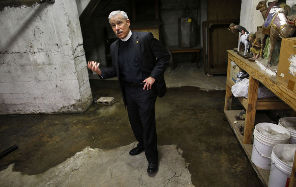  The Rev. Win Lewis shows how even on a sunny day, March 21, 2017, water can accumulate in the basement of Christ &amp; St. Luke's Episcopal Church in Norfolk, which stands just across the street from the flood-prone Hague. 