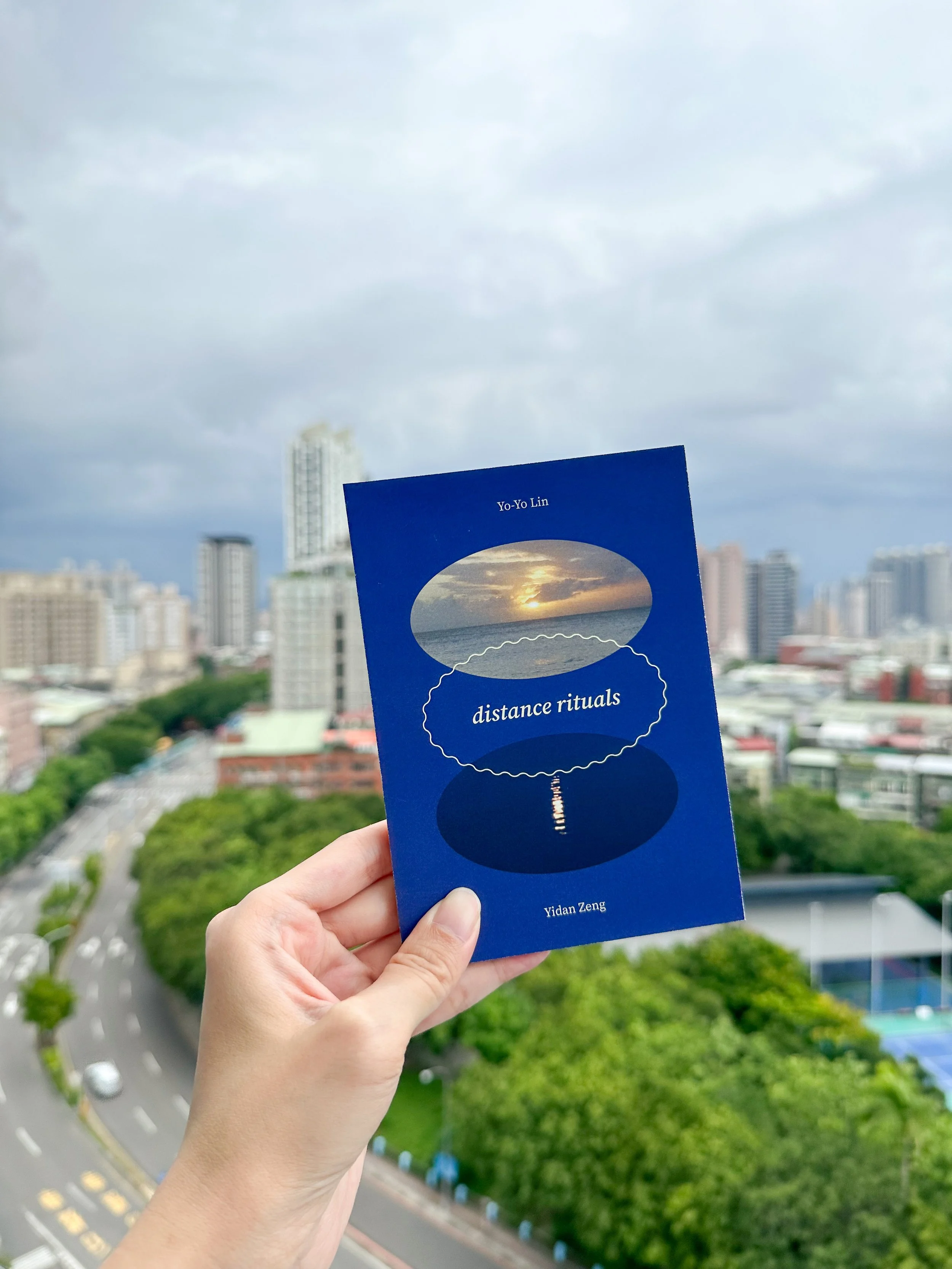 hand holding distance rituals zine over a cityscape in Taipei