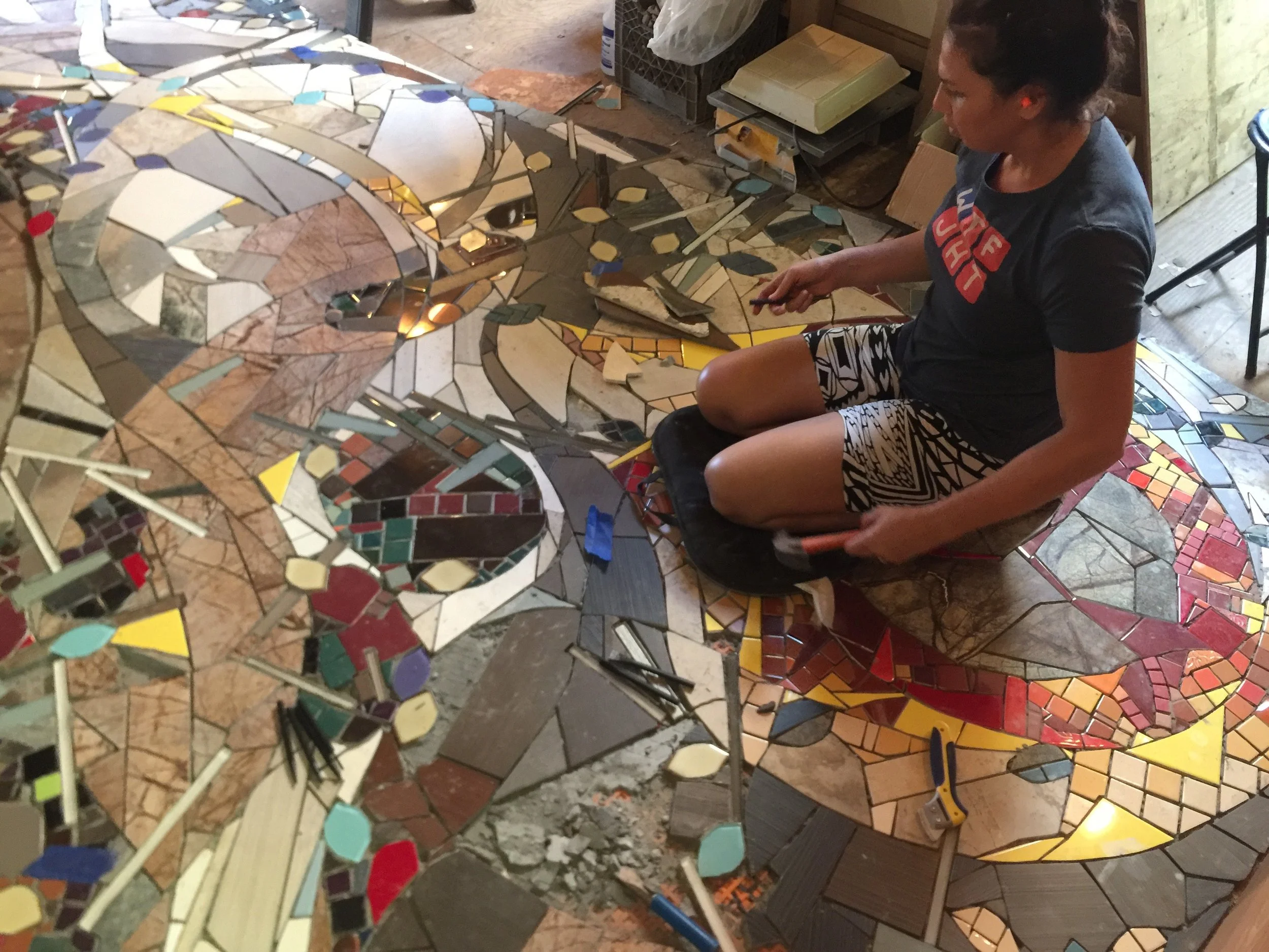 Above: Maya fills in remaining pieces of this biophilic floor mural which suggests fallen leaves and sticks strewn across a trail, cutting thru the living space. The dull flicker of flames emanating from the fire place that will be installed later where she is sitting, draw the eye to intentional sprinkles of yellow fallen across the floor. 