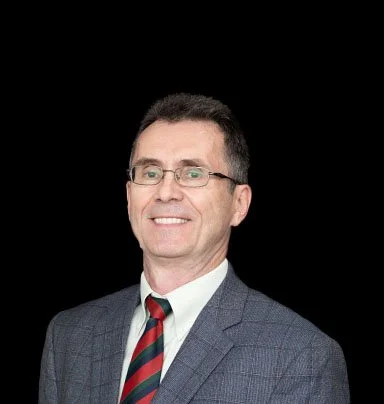 A professional man wearing glasses, a blue checkered suit, and a red and blue striped tie, smiling against a black background.