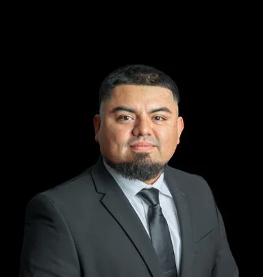 Portrait of a man in a dark suit, white shirt, and tie against a black background.