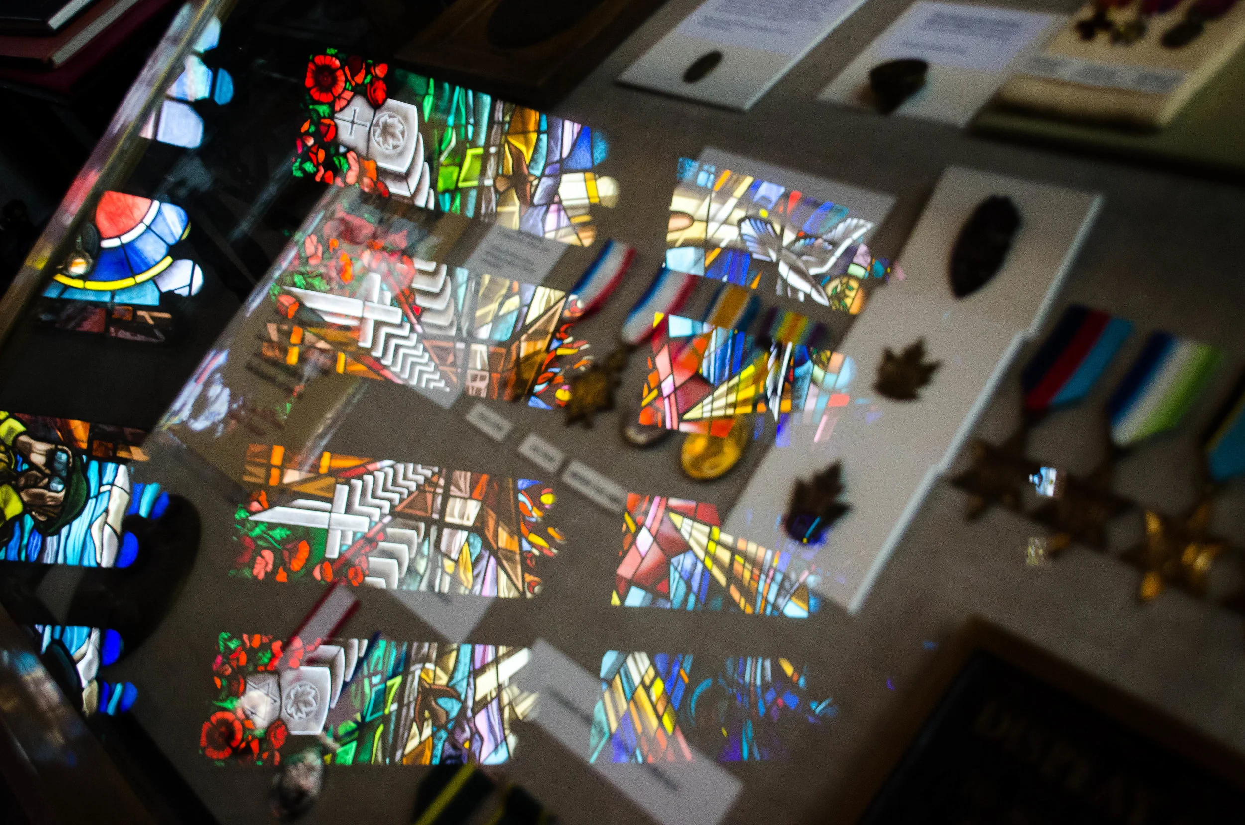 The twelve pane stain glass window depicting John McCrae's poem 'In Flanders Field' is reflected off of a display case inside the Memorial Room
