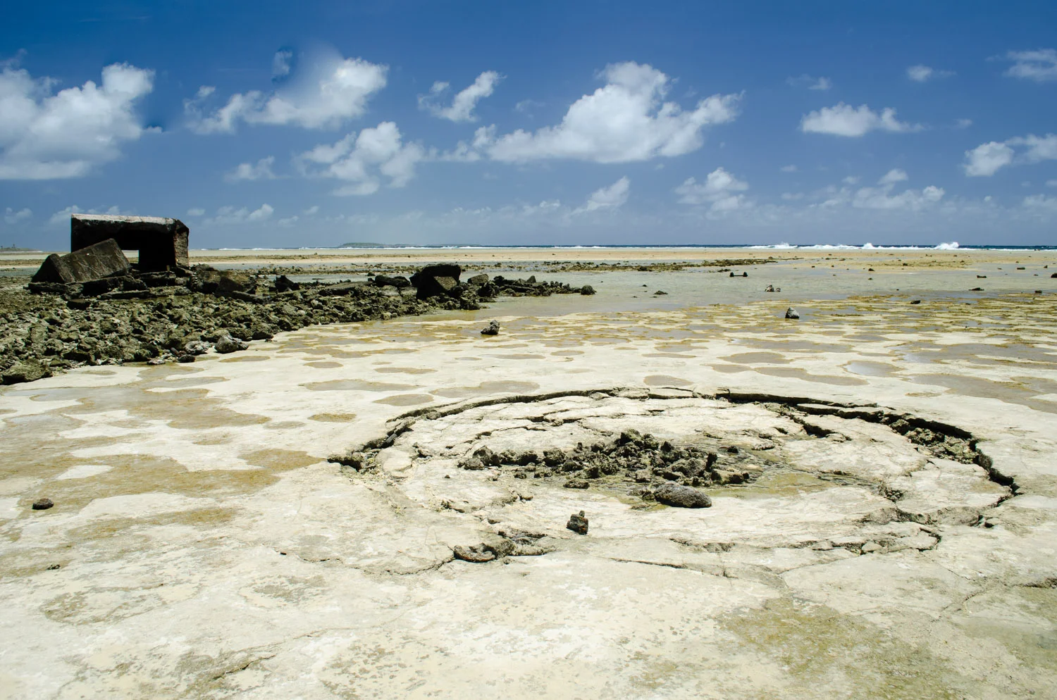 Low tide exposes this crater beside the remains of a bunker