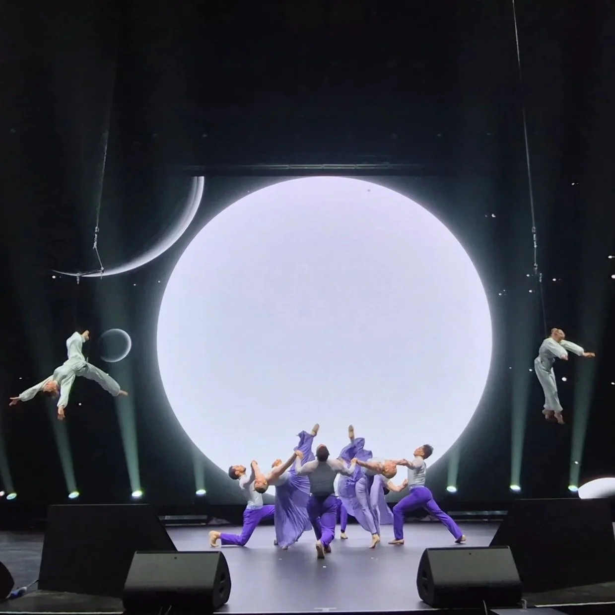Stage performance with large moon prop and ensemble of dancers in theatrical production