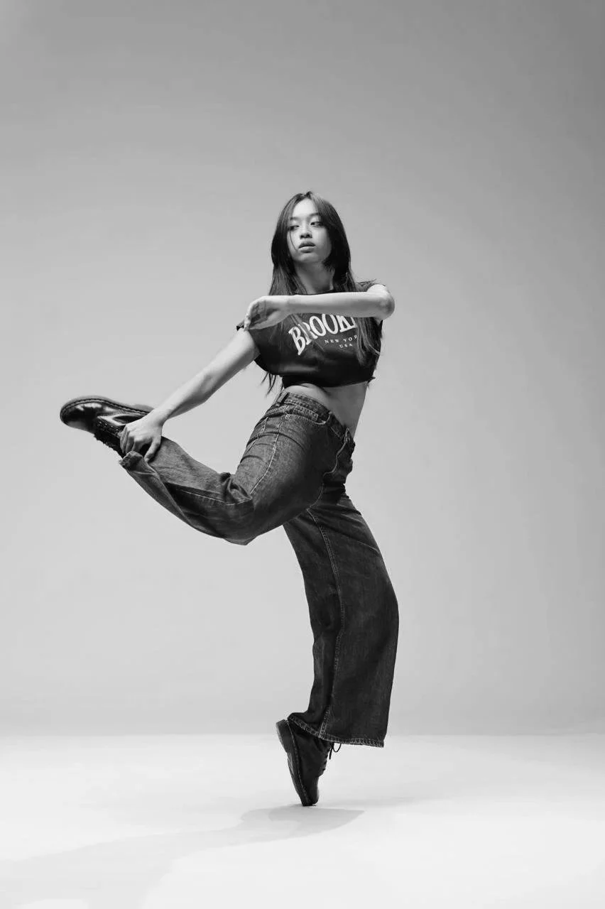 Person dancing in a dynamic pose, wearing a crop top and jeans. Rei Co