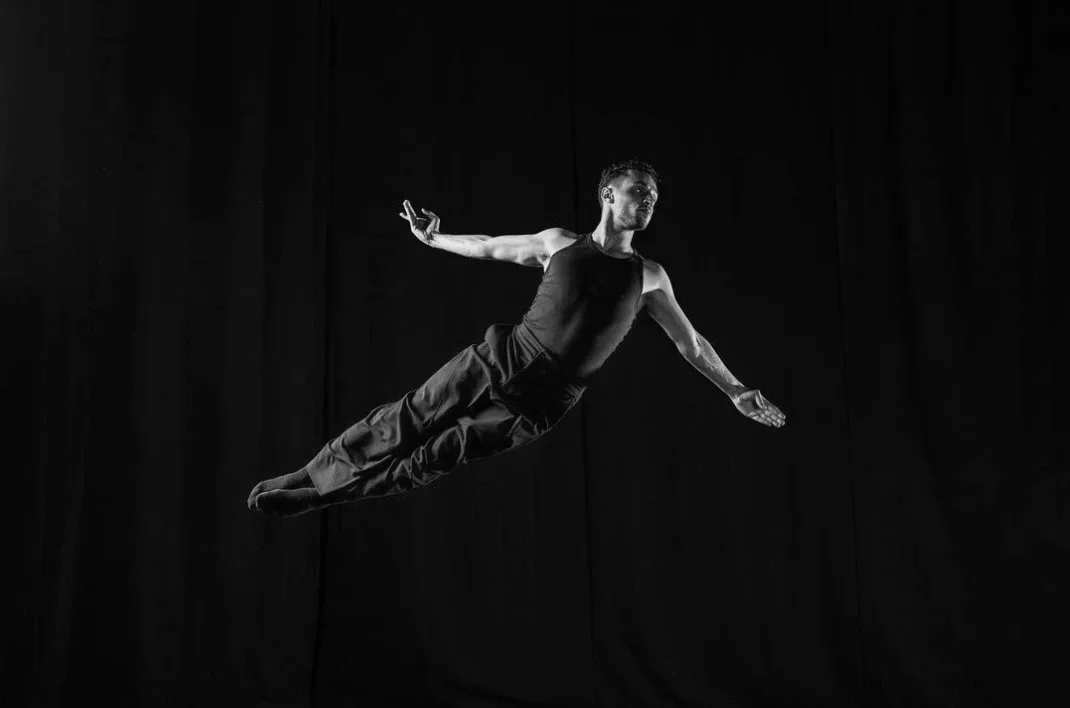 Dancer in mid-air leap on dark background Hassan Alresheiq