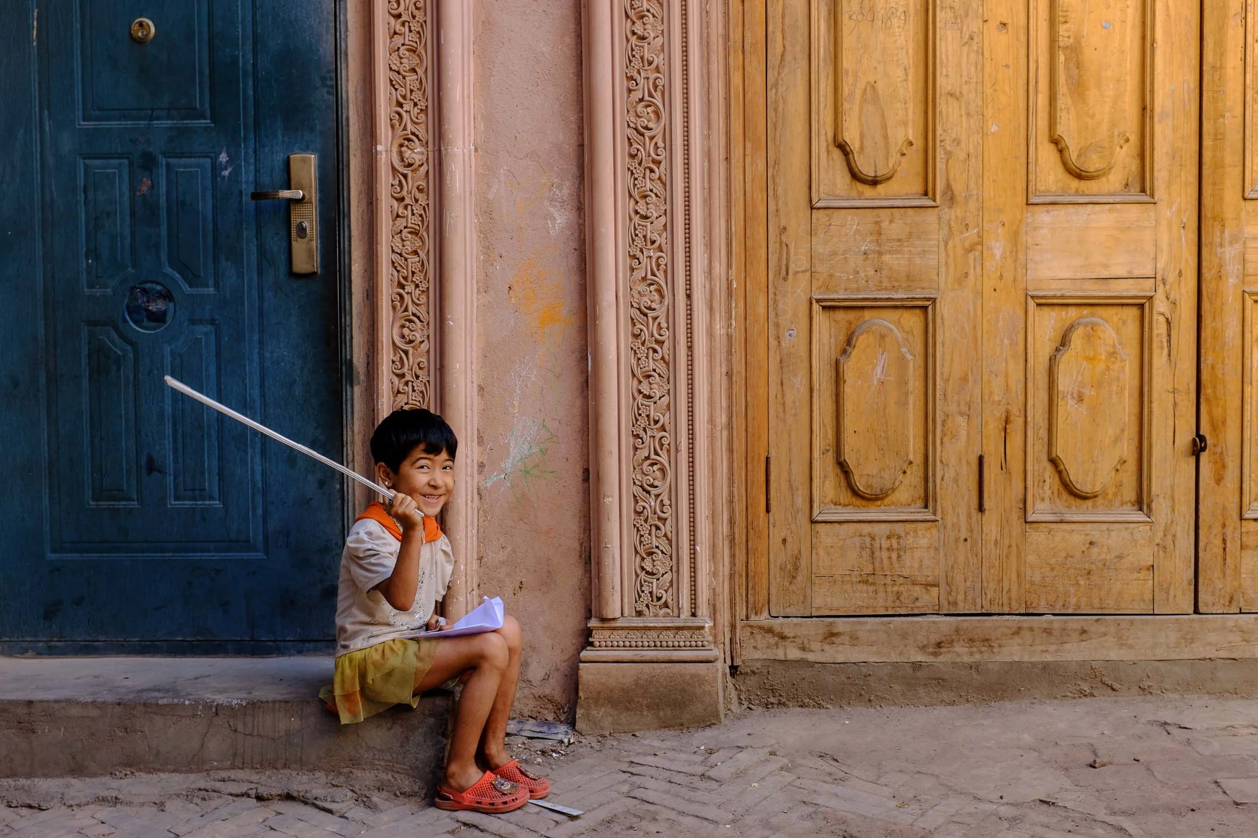 A young girl smiling on a stoop in one of the wandering alleyways of Kashgar's old town