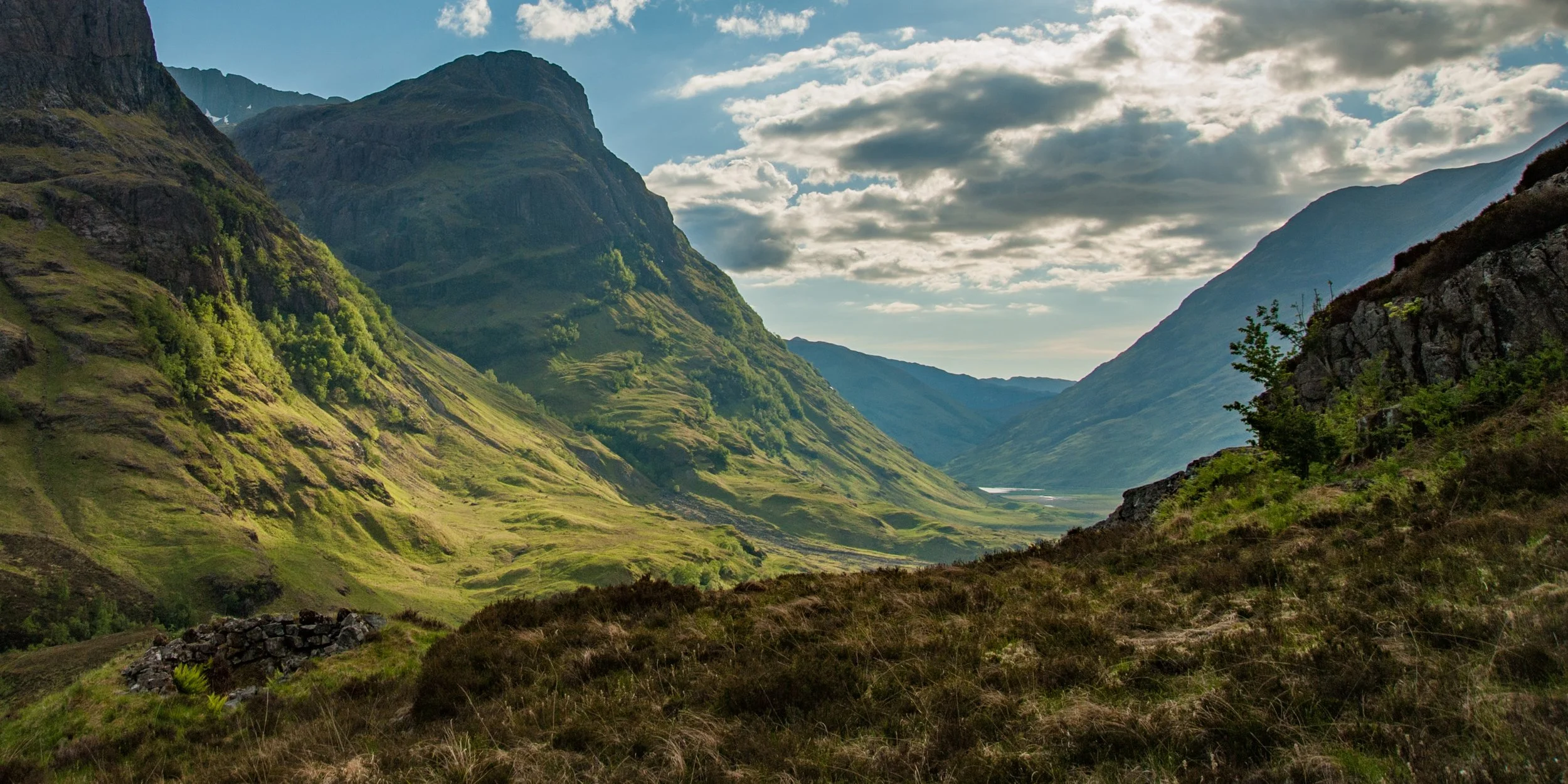 View of valley in Glencoe Scotland in morning with shadows and road snaking through to lake in distance