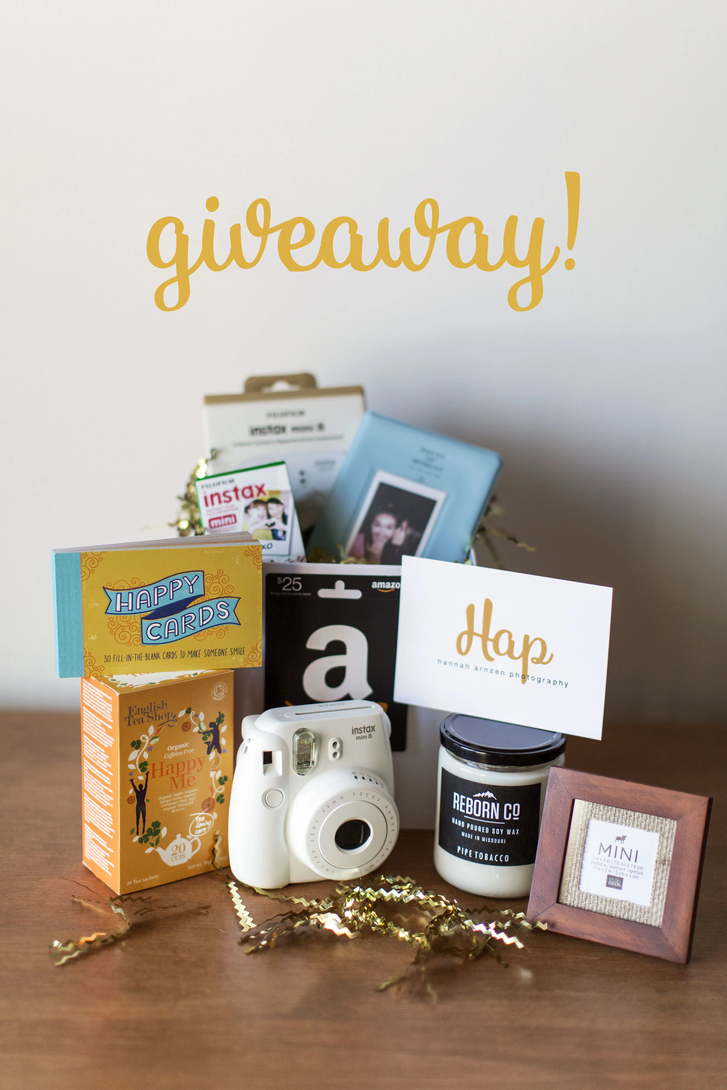Giveaway items include the following: A BRAND NEW Fujifilm instax mini 8 camera, colored film for the instax mini 8, (1) photo album for your polaroids, (1) $25 gift card to Amazon, (1) HAPPY CARDS book, (1) box of organic Happy Me tea, (1) Pipe Tobacco soy wax candle from REBORN CO, (1) $50.00 gift certificate towards a HAP photo session, and (1) wooden photo frame with YOUR entry photo! 