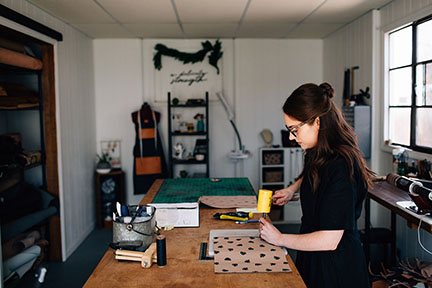 Megan hand punching stitch holes on a leather bag in the Stitch &amp; Shutter Studio 