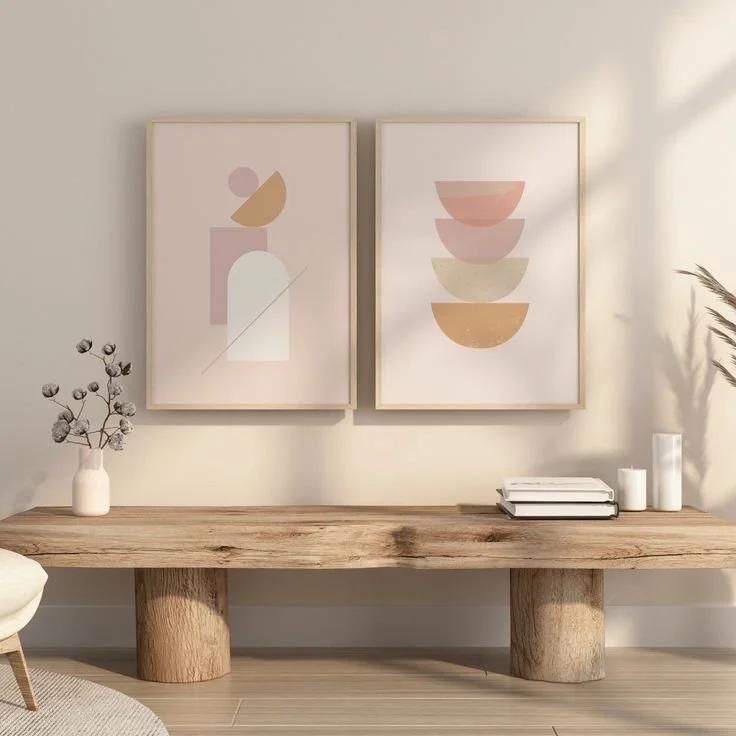 Minimalist living room decor with two geometric abstract art prints hanging above a rustic wooden console table, decorated with a vase of cotton stems, stacked books, and white candles.