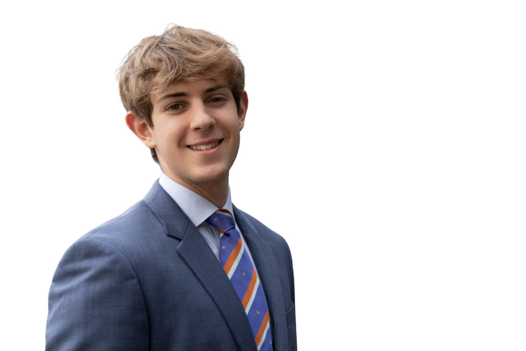 A young man with light brown, wavy hair smiling, dressed in a blue suit with a collared shirt and a colorful striped tie, standing against a plain white background.