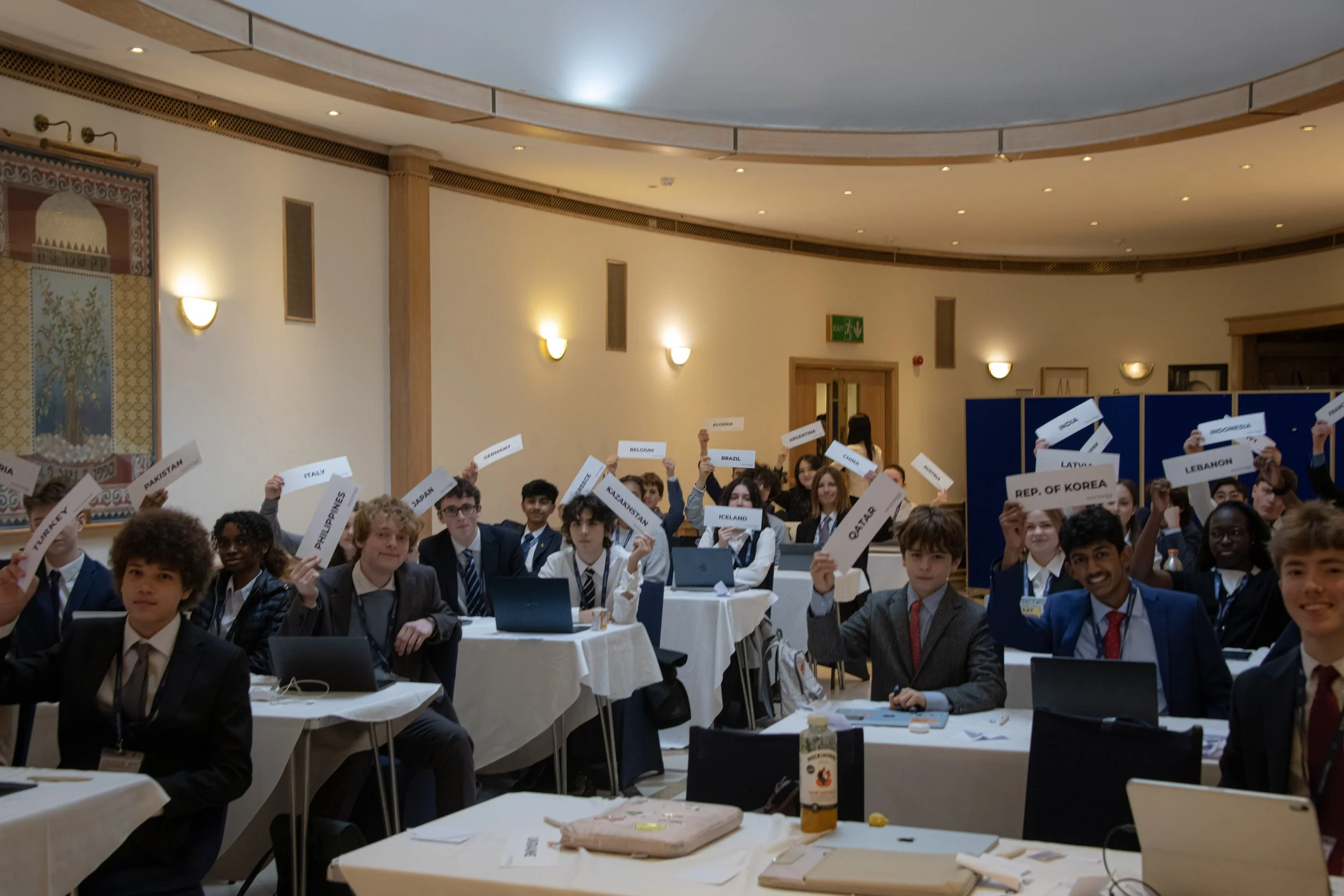 Students at a Model United Nations conference holding name cards from different countries in a conference room.