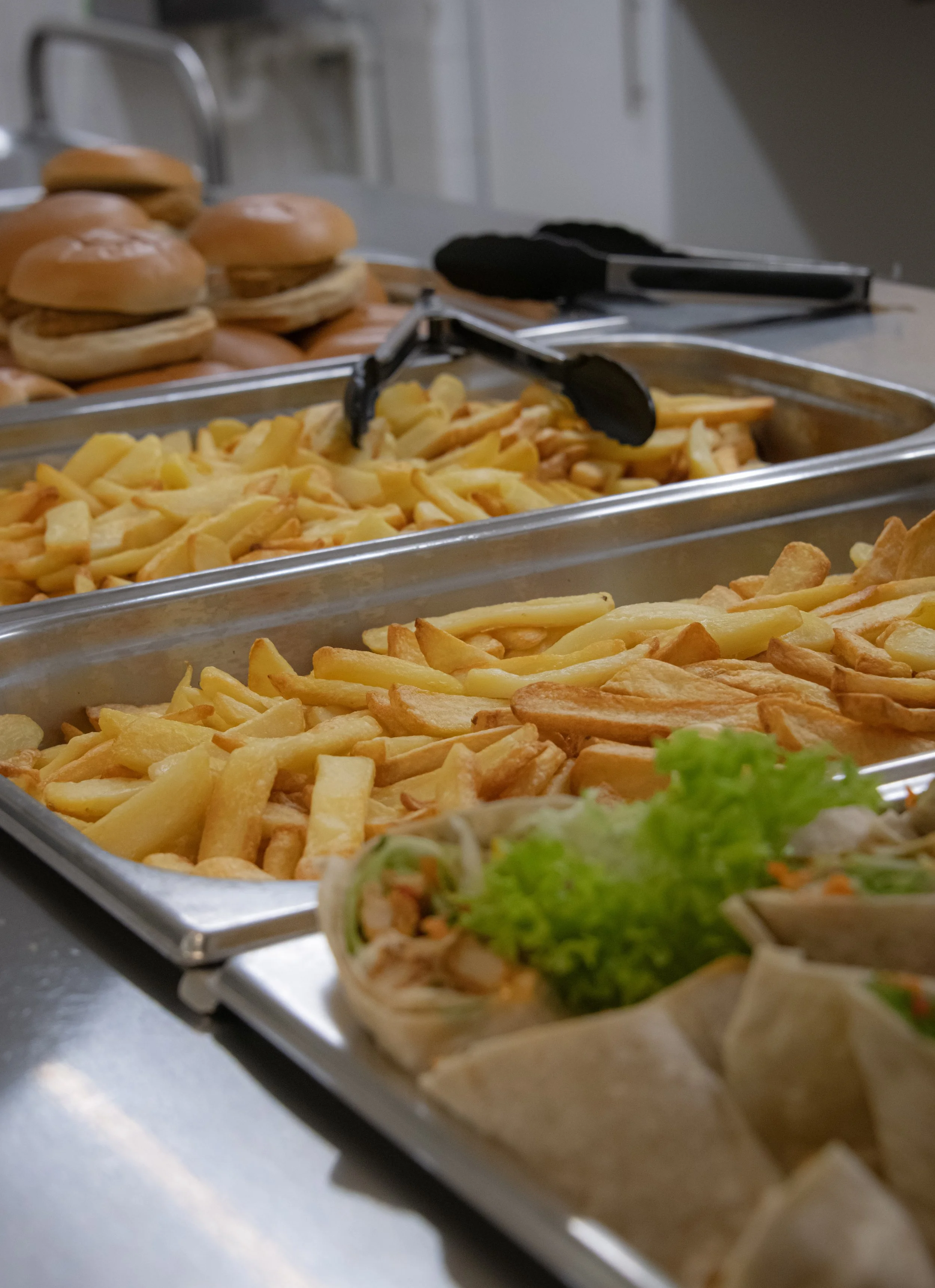 Buffet with trays of French fries, sandwiches, and a small salad with lettuce in the foreground.