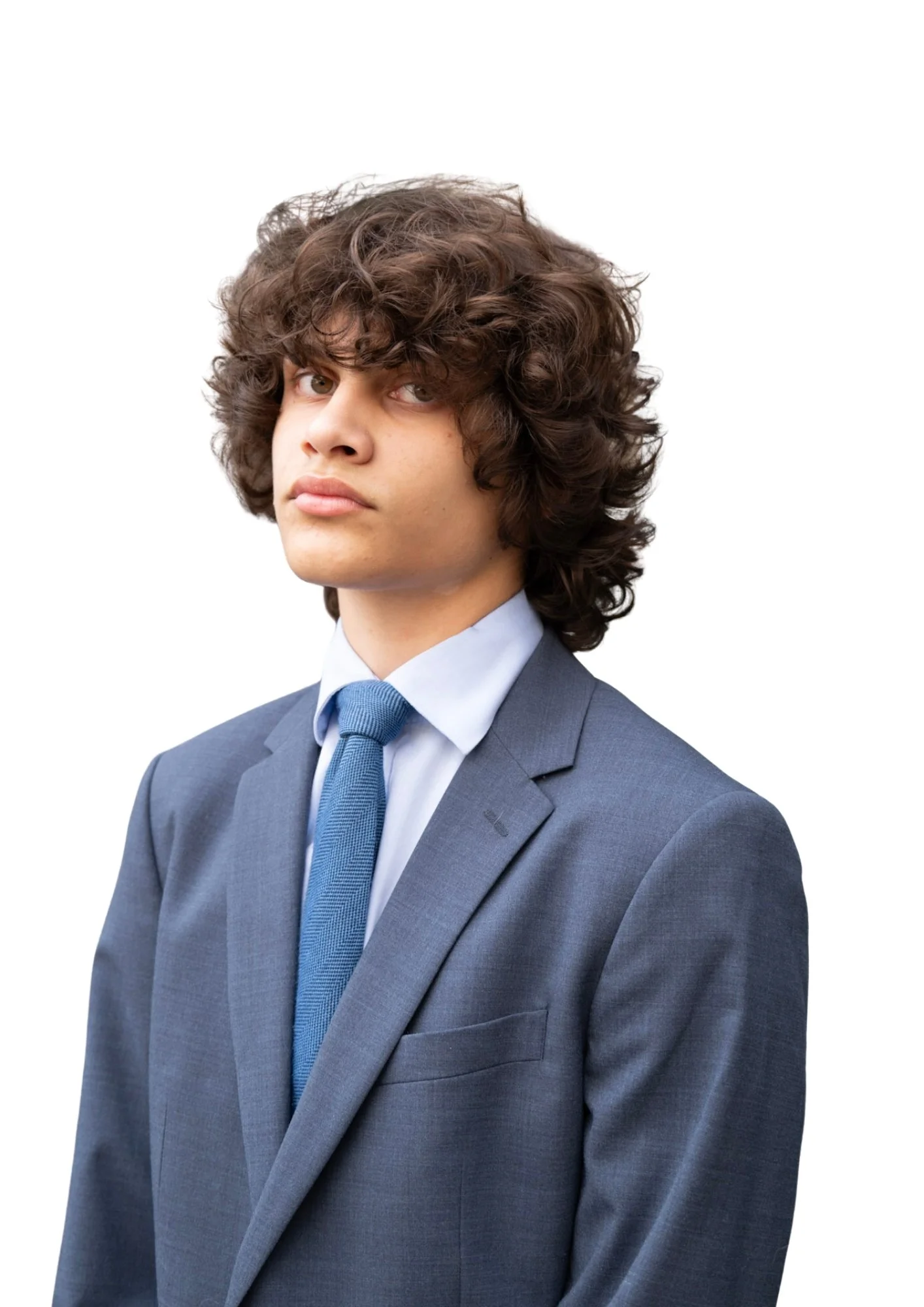 A young man with curly brown hair wearing a blue suit, light blue shirt, and matching tie, standing against a white background.