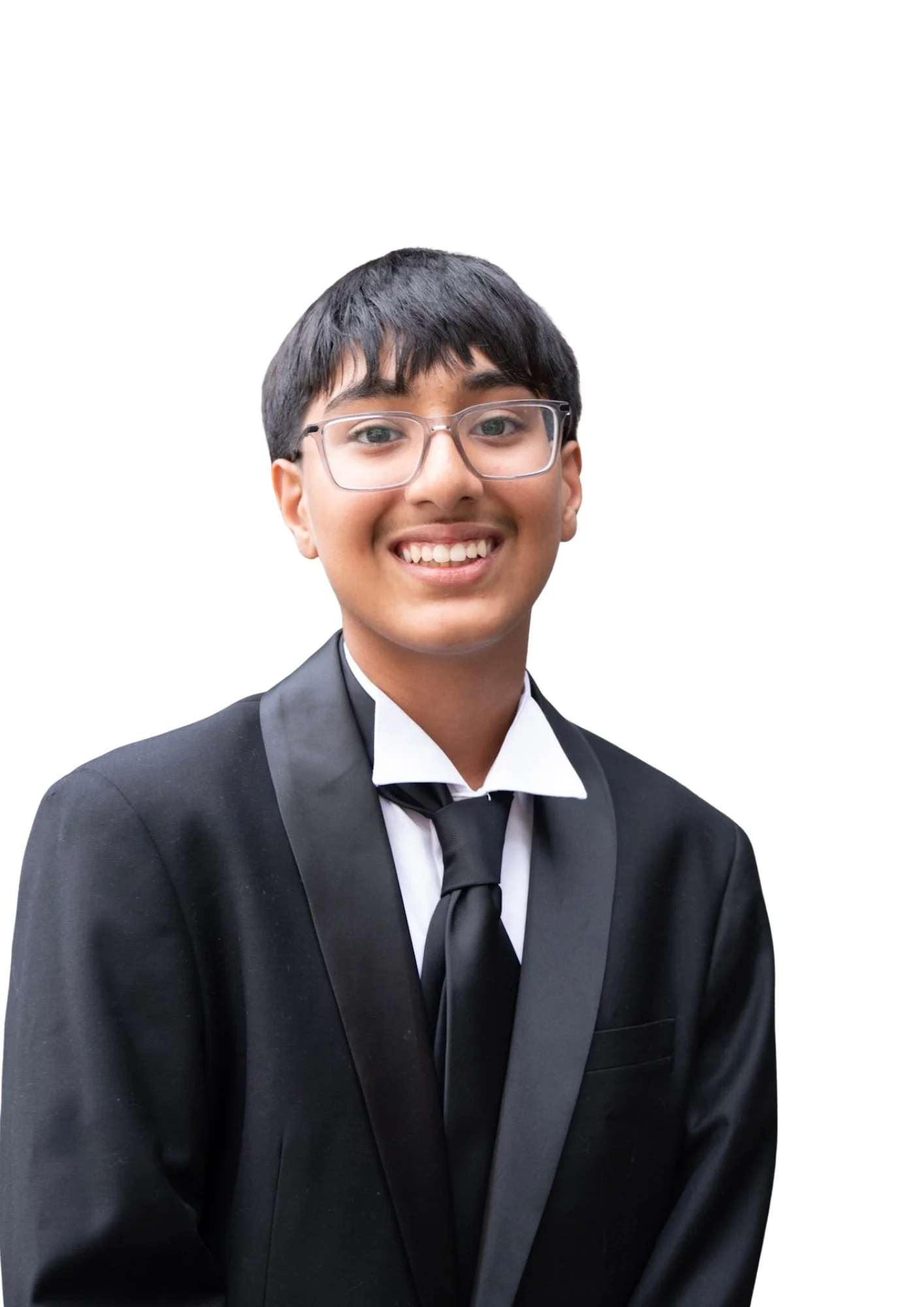Young man in tuxedo smiling, wearing glasses, against a white background.