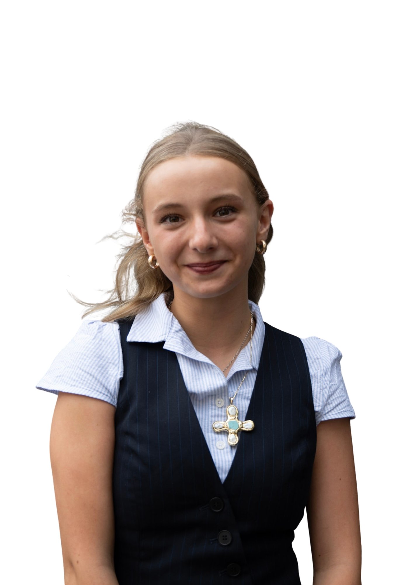 A young woman with blonde hair styled in loose waves, wearing a blue pinstripe vest over a collared shirt, gold hoop earrings, and a large cross necklace, standing against a plain white background.