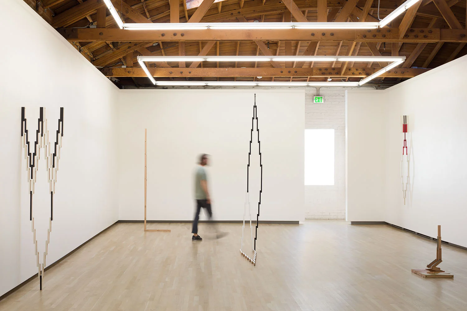 In Four Acts, installation view. Shulamit Nazarian Gallery, LA, 2018 In Four Acts features a series of new works that occupy the floor and walls of the gallery. Each sculpture originates in a flat, compact state, but is modular and has the potential to expand to form multiple variations of itself. The exhibition title refers to the dynamic state of the exhibition. During the course of the show, the works gradually unfold from minimal configurations into more elaborate adaptations. Each sculpture will change four times over the course of the exhibition, with each modification resulting in a new visual landscape. The sculptures are constructed from multiple segments of precisely-cut oak hinged together with brass hardware. The faces of each segment are coated with paint and lacquer, shifting subtly through spectrums of color. As the viewer moves around the pieces, parts appear to either recede or protrude, while the materials used for these works echo the materials used in the gallery’s architecture, creating a dialogue and a growing tessellation within the space. This new body of work marks a shift in Israel’s practice, emphasizing the idea of sculptures existing in a changeable state. By departing from a fixed form as the basis for his works, Israel proposes sculptures that are the sum of multiple possibilities, creating an evolution—with regards to shape, scale, and pattern—within a single artwork.