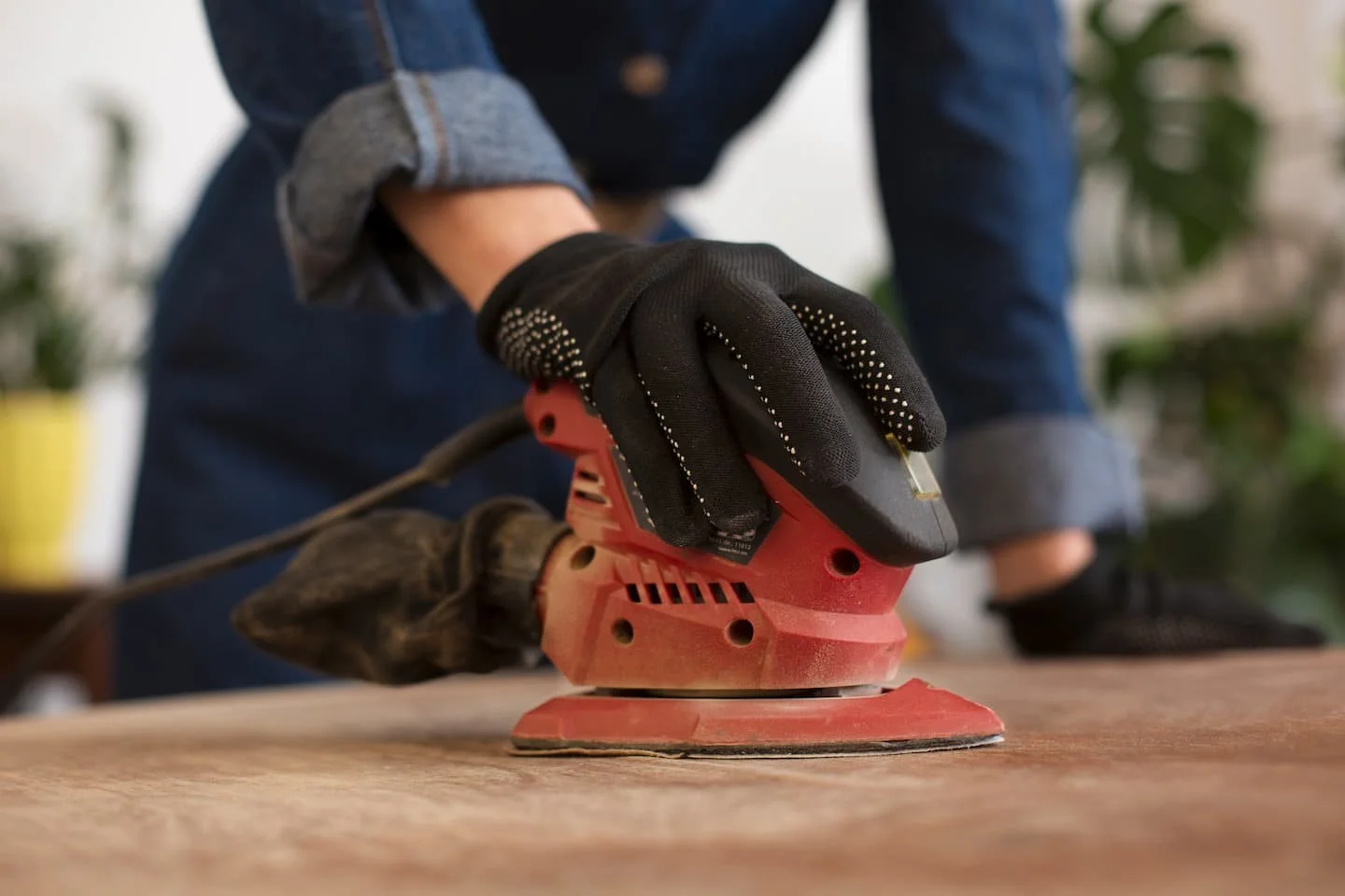 Image of a person sading a piece of wood with a handheld sanding machine
