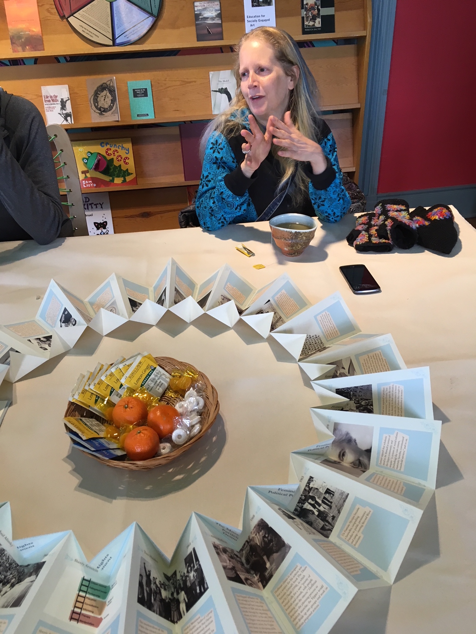   The Hum: Members of the community add to the table (fruit and tea basket). In the foreground, an interactive timeline of key Social Practice documents, influences, and artwork.    The Hum  is a socially engaged artwork that integrates and adapts th