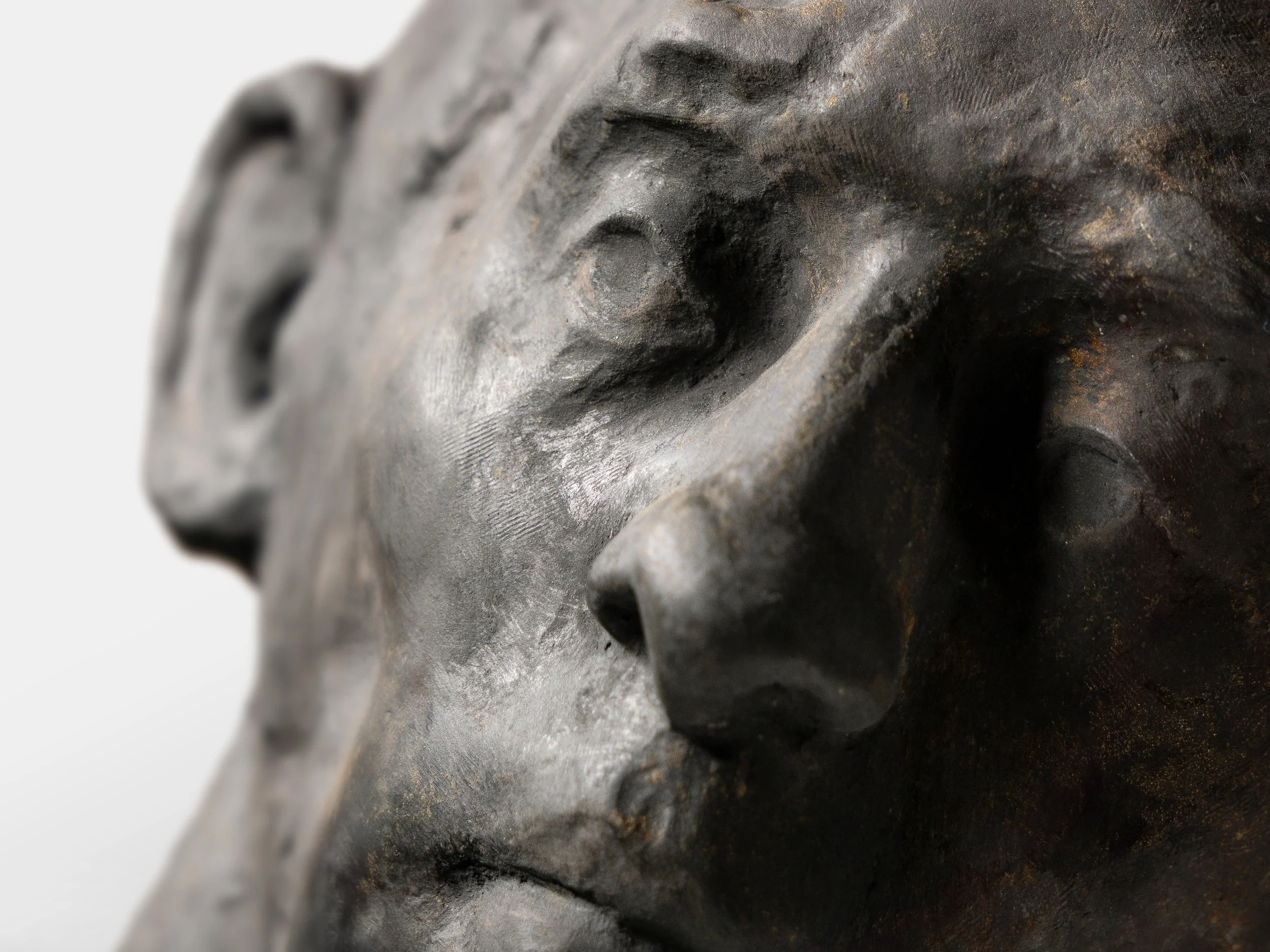 Close-up of a metal sculpture or mask showing a person's face with detailed facial features.
