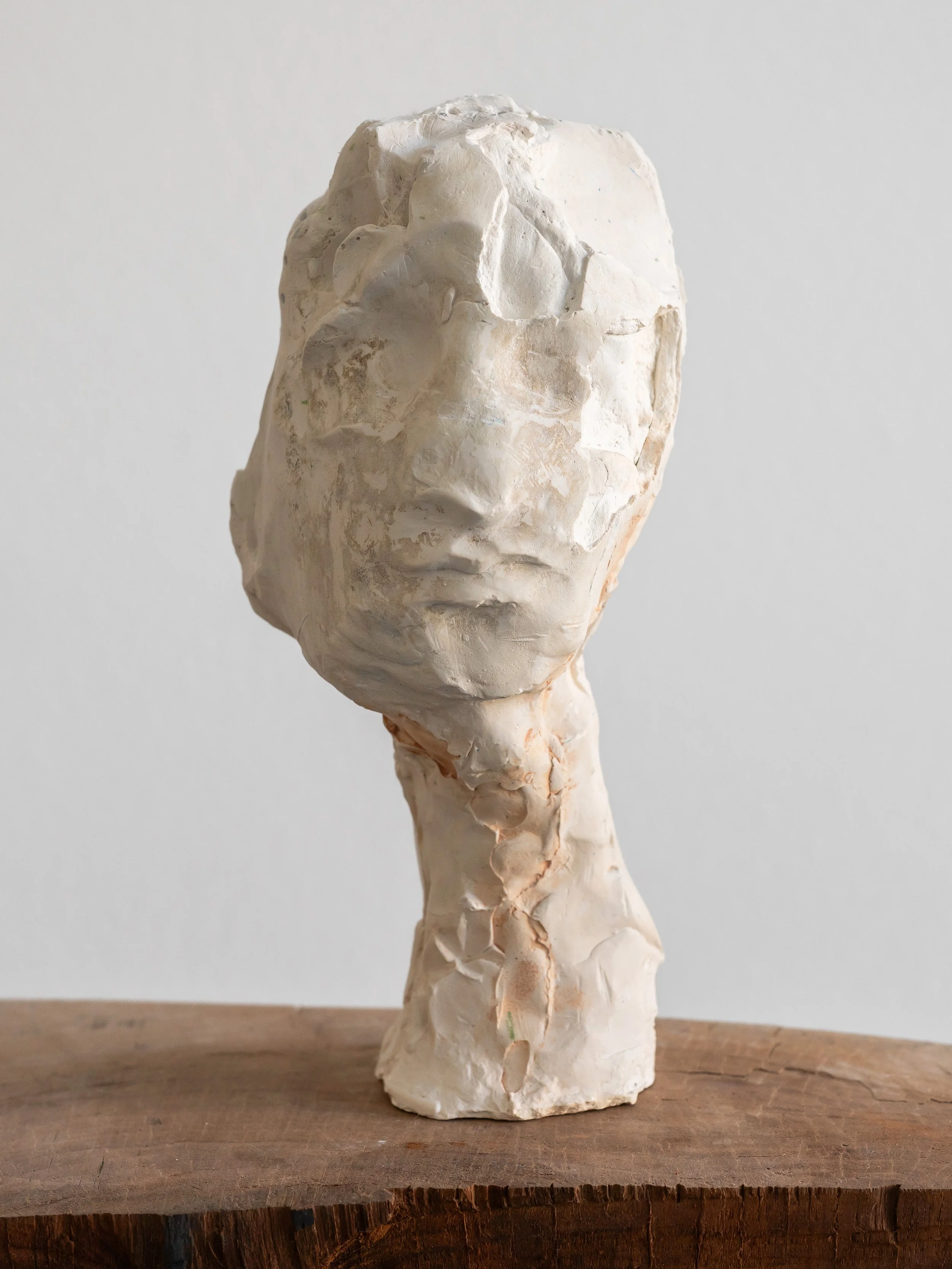 White abstract sculpture of a human face and neck on wooden base.