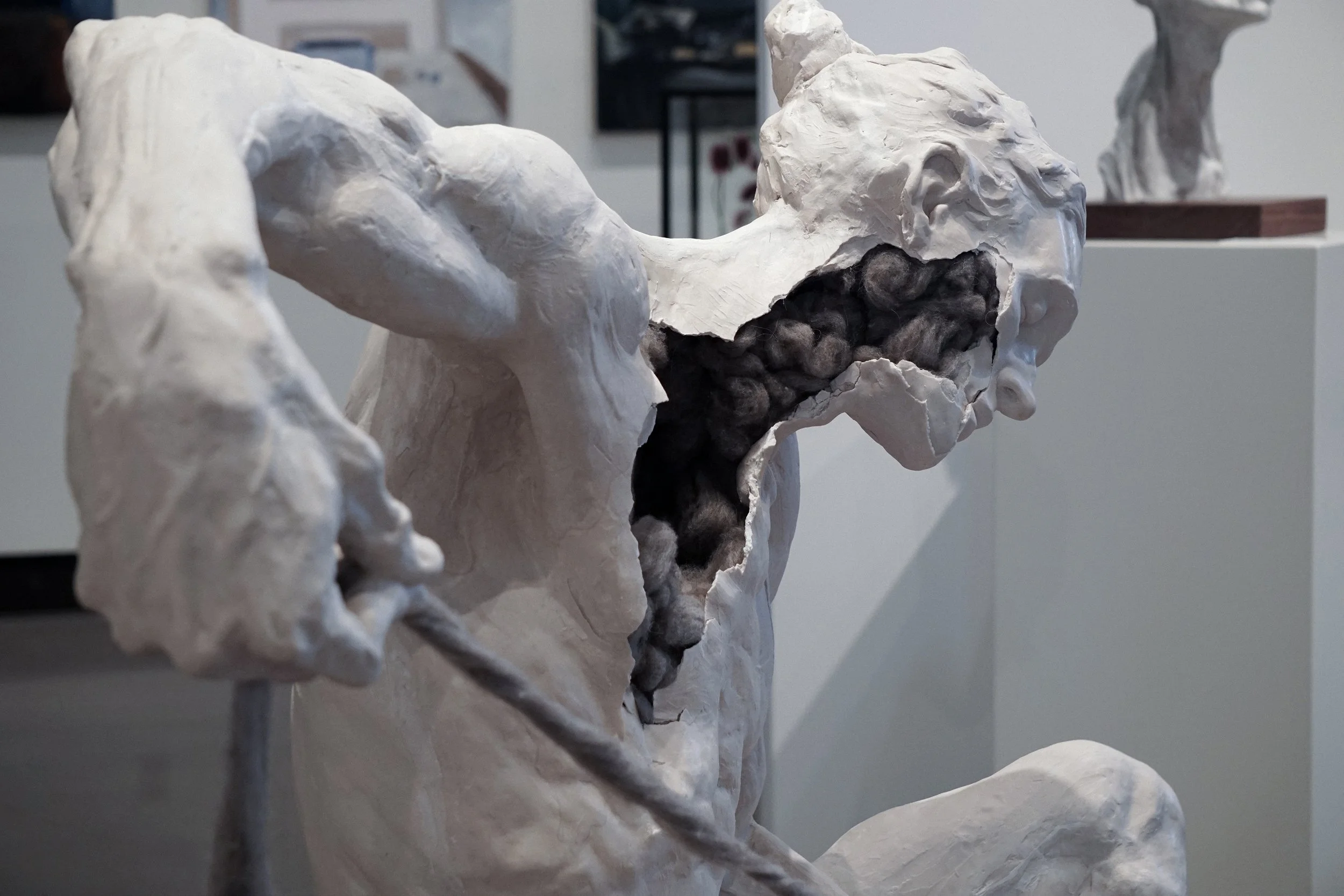 A sculpture of a person with a large open mouth, showing dark, woolly material inside, made from a pale, stone-like material.