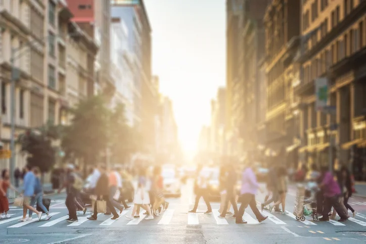 Anonymous-group-of-people-walking-across-a-pedestrian-crosswalk-on-a-New-York-City-street-with-a-glowing-sunset-light-shining-in-the-background-813211754_727x485.jpeg