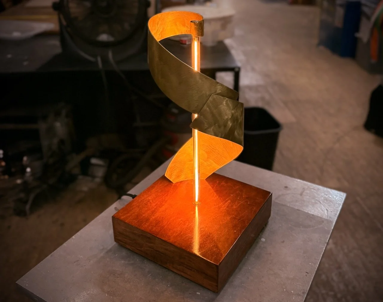 Helix One light sculpture glowing warmly, the brass spiral reflecting a soft, golden light against a high-luster wooden base