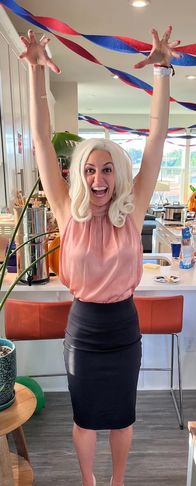 Lo Myrick as Rebecca Welton from Ted Lasso in a blush pink top, recreating the make myself big confidence pose