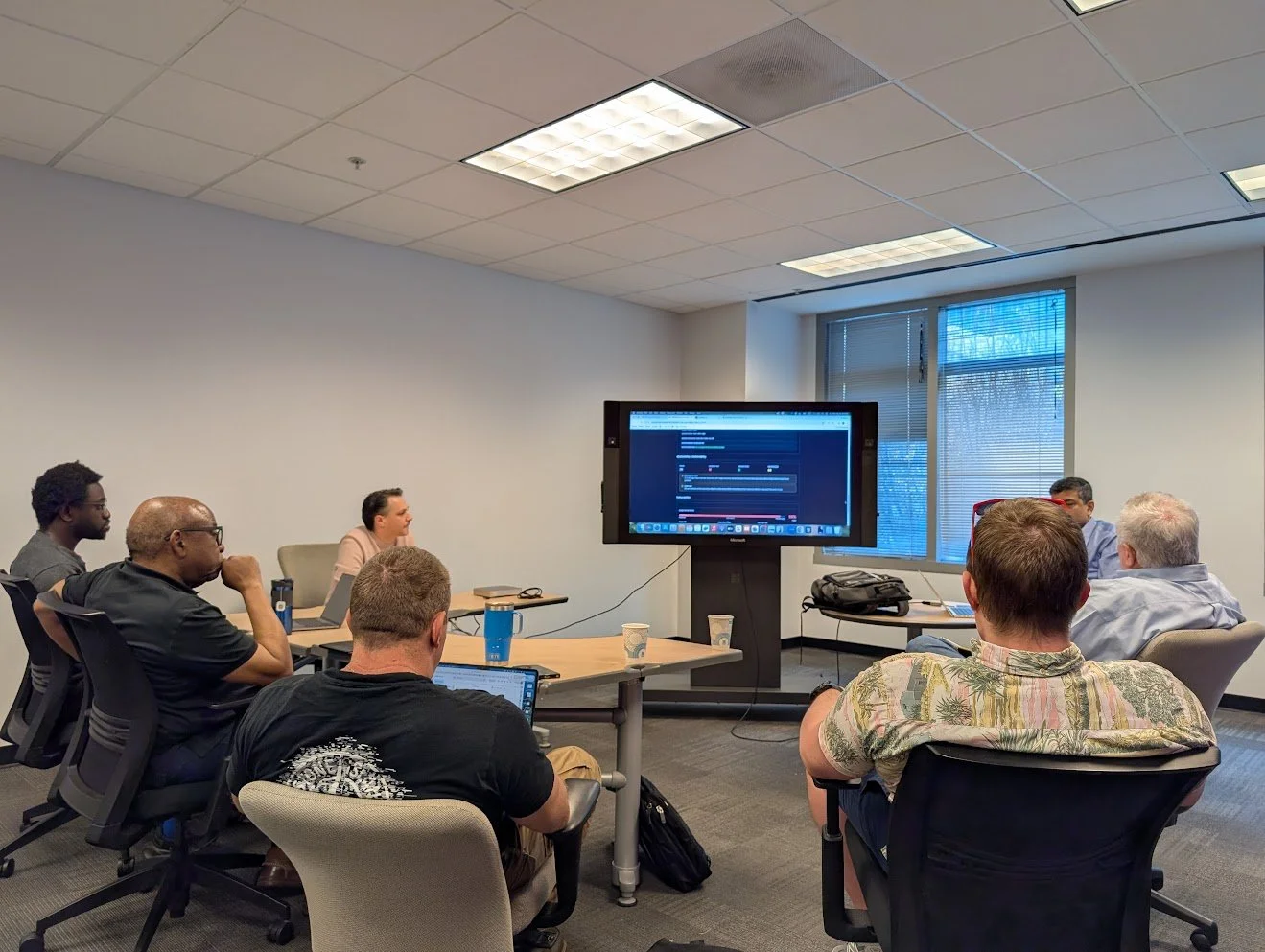 Image shows a room full of people watching a presentation at ATDC's Mond(AI)y Coffee. The groups is discussing in front of a TV screen. Credit: Mond(AI)y Coffee.