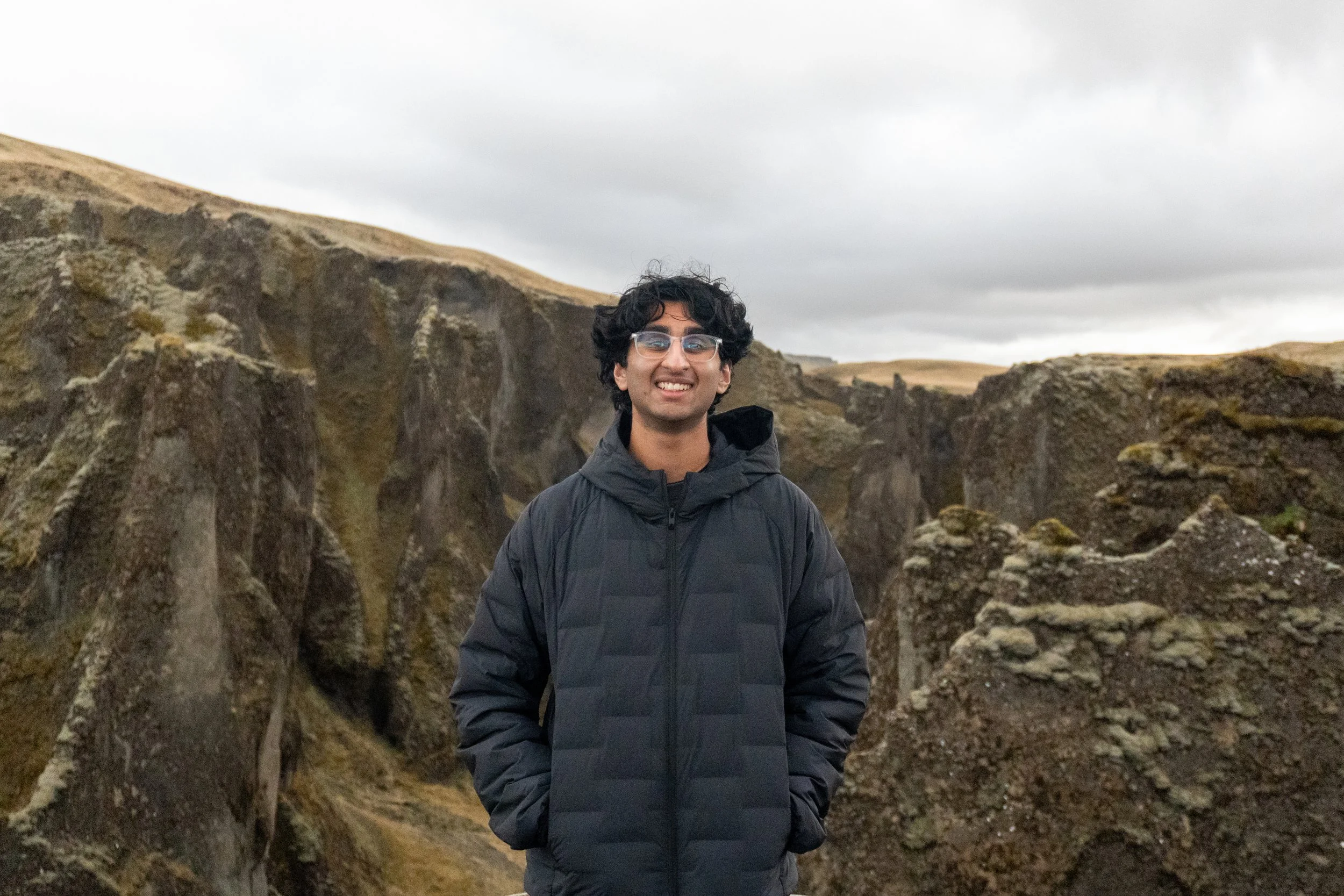 Photo of Mehul Jasti in a winter coat standing in front of a rocky, moss covered landscape with a gray sky. Jasti is the developer of JustLmk. Source: Mehul Jasti/JustLmk.