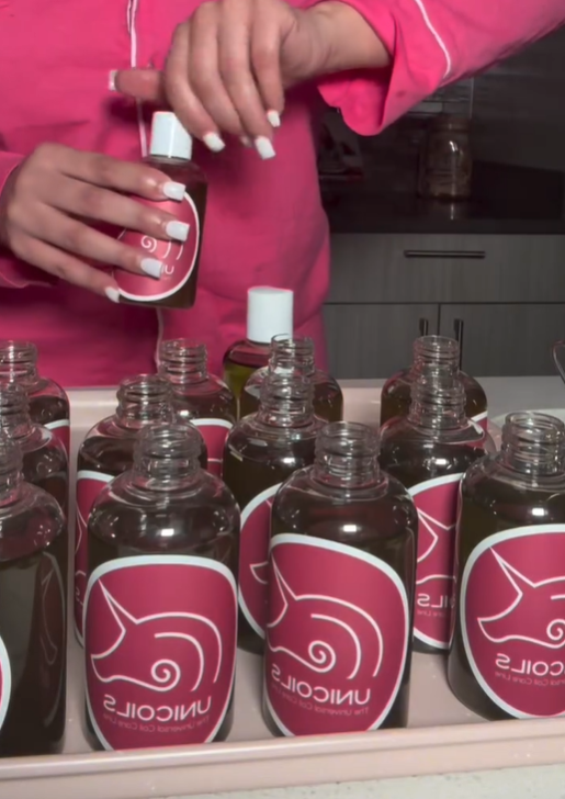 Close up photo of Dajheonna Perry preparing and bottling Unicoils products. The bottles have a pink sticker label with the Unicoils logo. Source: Unicoils/Instagram.