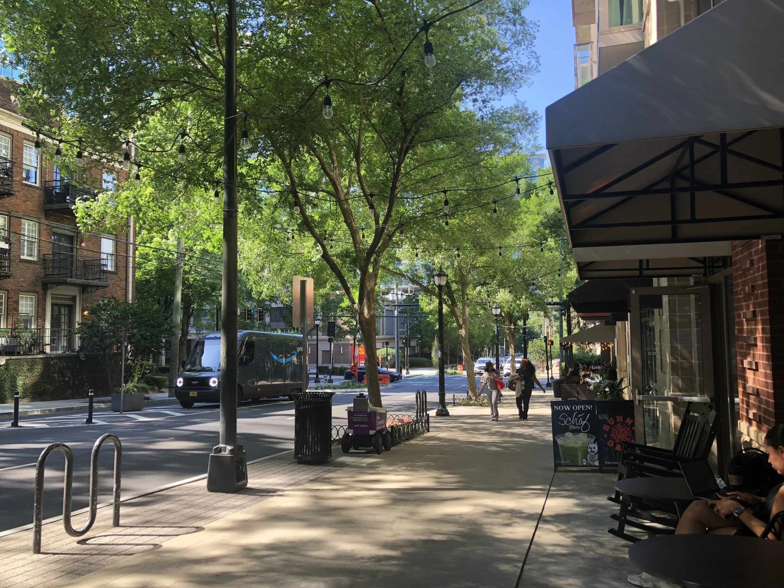 Photo of a smaller city street with trees, sidewalk, storefronts, pedestrians, and road. Photo: Pearl Kaplan/Tech Square ATL.