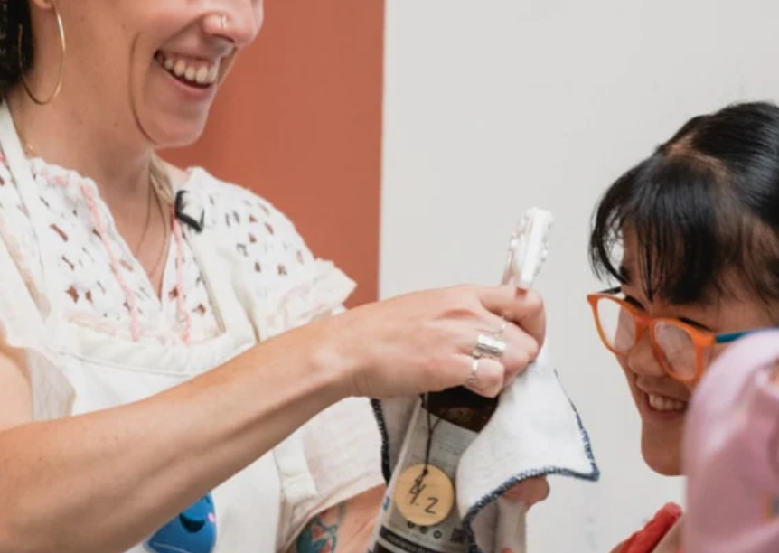 Photo of Veronica Apecena and a child smiling and refilling a bottle of home cleaning product. Source: Joyful Jarra.