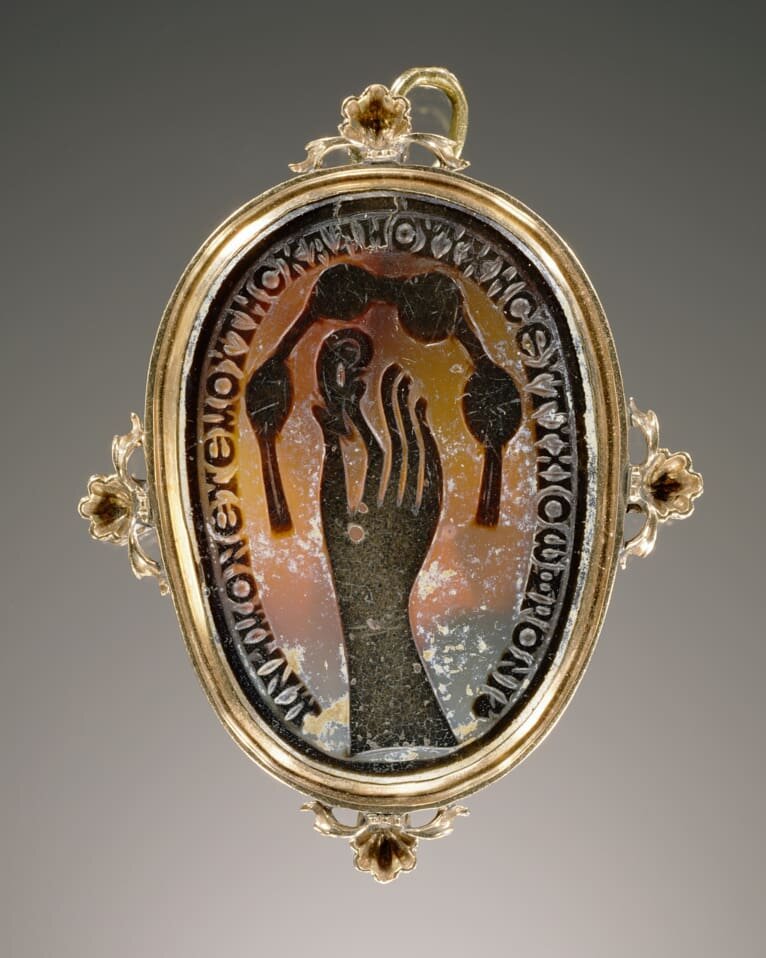 Roman agate cameo dating to the 5th century AD set in a modern gold setting. The cameo depicts a hand pinching an ear. Above is a knotted scarf or diadem. The inscription is Greek and reads: &ldquo;Remember me, your dear sweetheart, and fare well, So