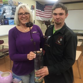 Senior Metal Fabrication student, Jacob Thall, presents social studies teacher, Lin Gross with bronze metal roses.