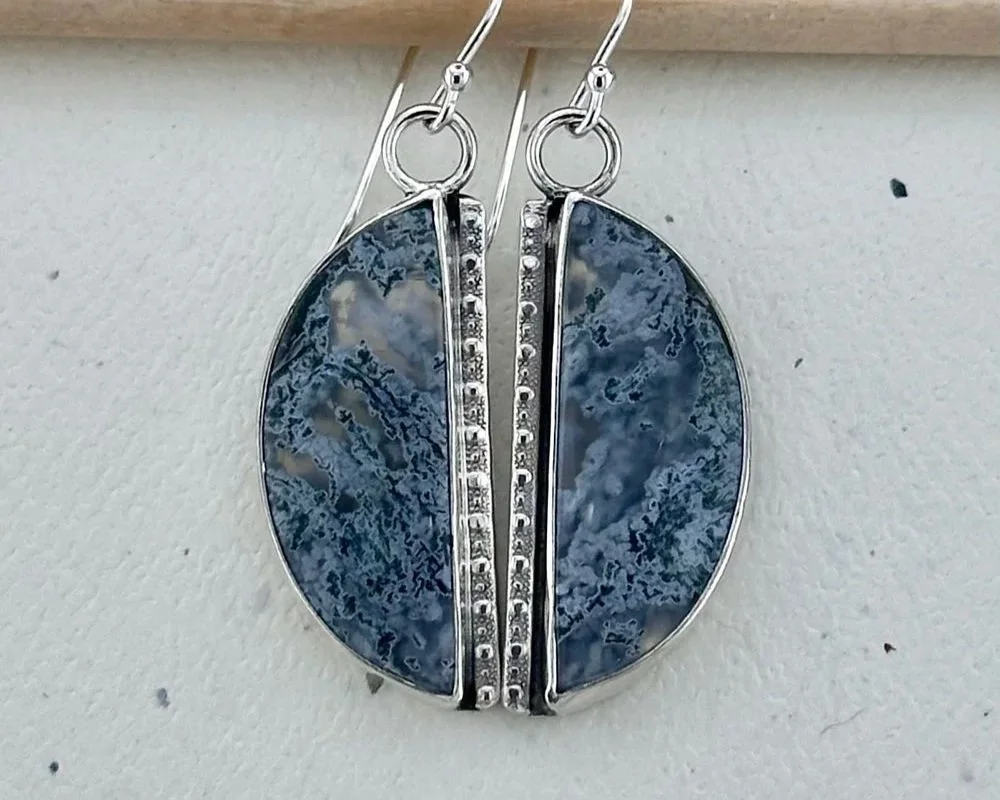 Silver earrings with oval blue and gray marbled stones and vertical row of small clear gemstones.