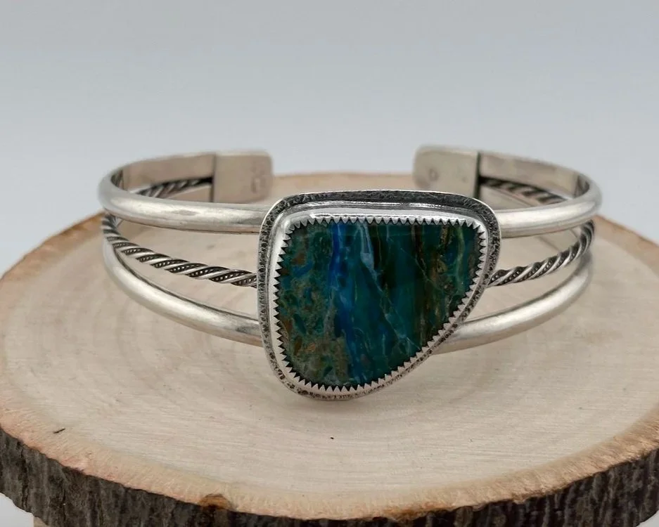 Silver cuff bracelet with a large triangular turquoise stone, resting on a wooden surface.