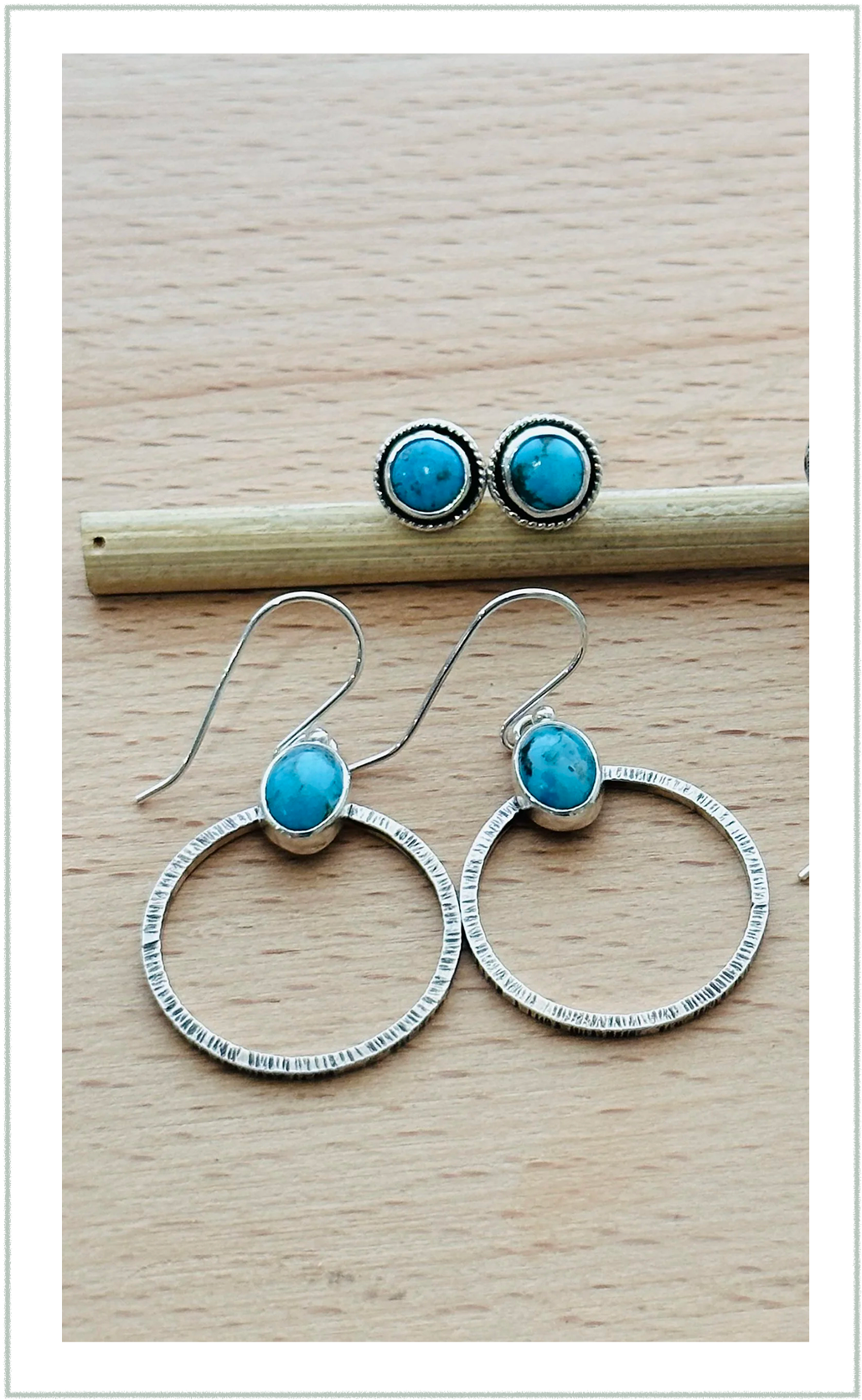 A pair of turquoise stone earrings and a pair of turquoise stone stud earrings arranged on a light wooden surface with a small wooden stick underneath.