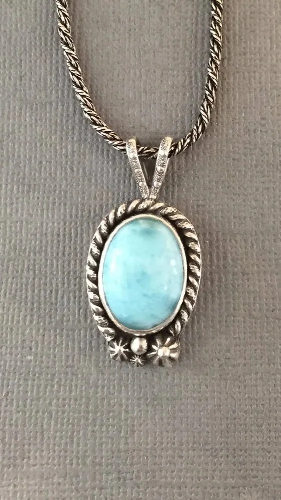 Silver necklace with a large oval turquoise pendant decorated with star-shaped and spherical accents on a textured gray background.