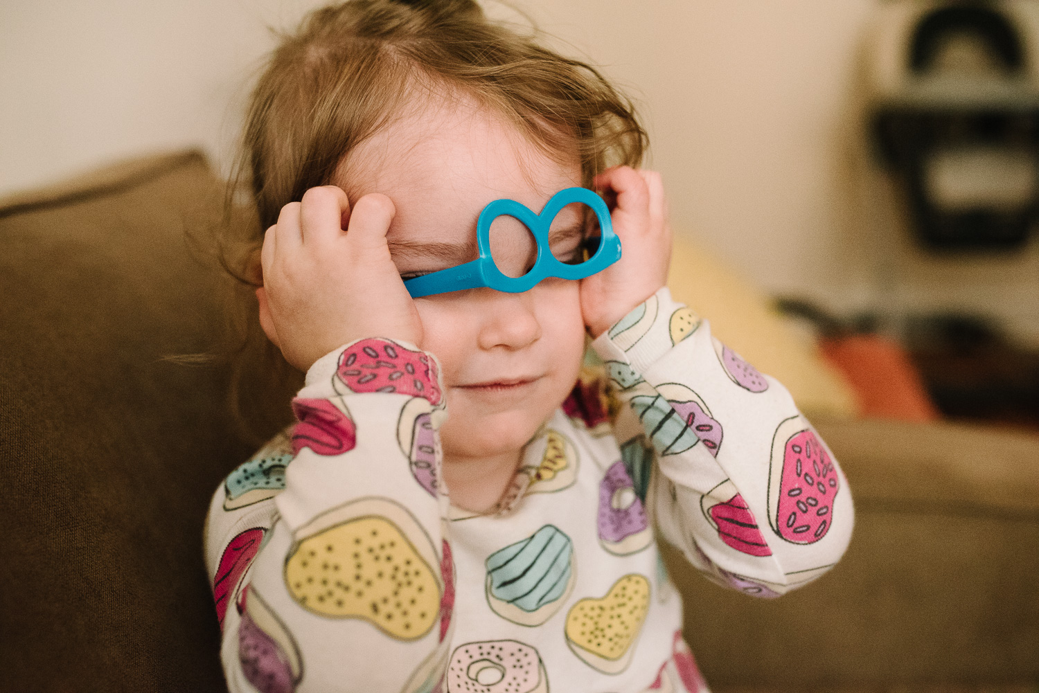 Little girl in donut pajamas puts on a blue pair of plastic glasses upsidedown