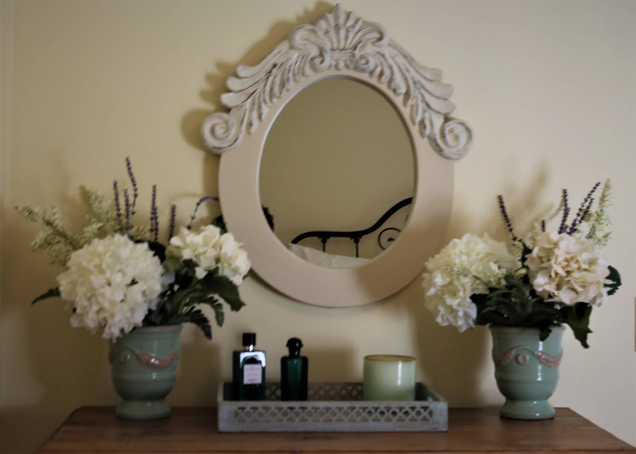 You can easily artfully layer a small space such as a dresser top. Here we flanked the antique mirror with matching vases of silk flowers. Then added a small tray for trinkets. Using different shades of neutral colors adds to the continuity. The small sprigs of lavender in the flowers adds a pop of color. 