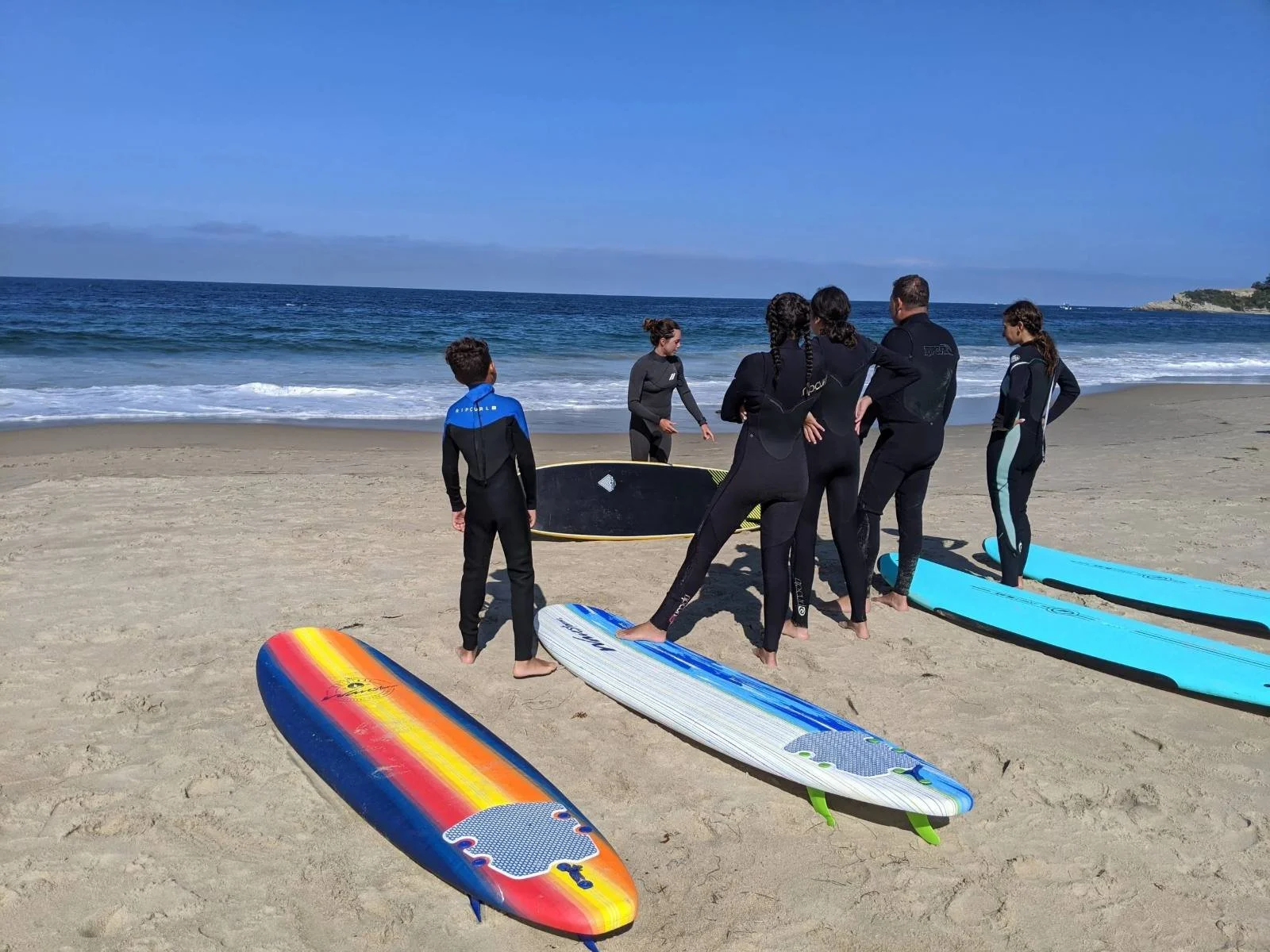 Surf lesson group in wetsuits with surfboards on the beach