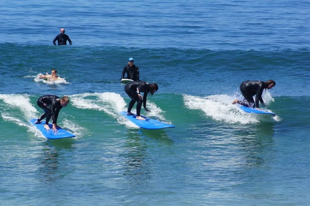 Corporate surf lesson group all standing up on one wave at Monarch Beach, Dana Point