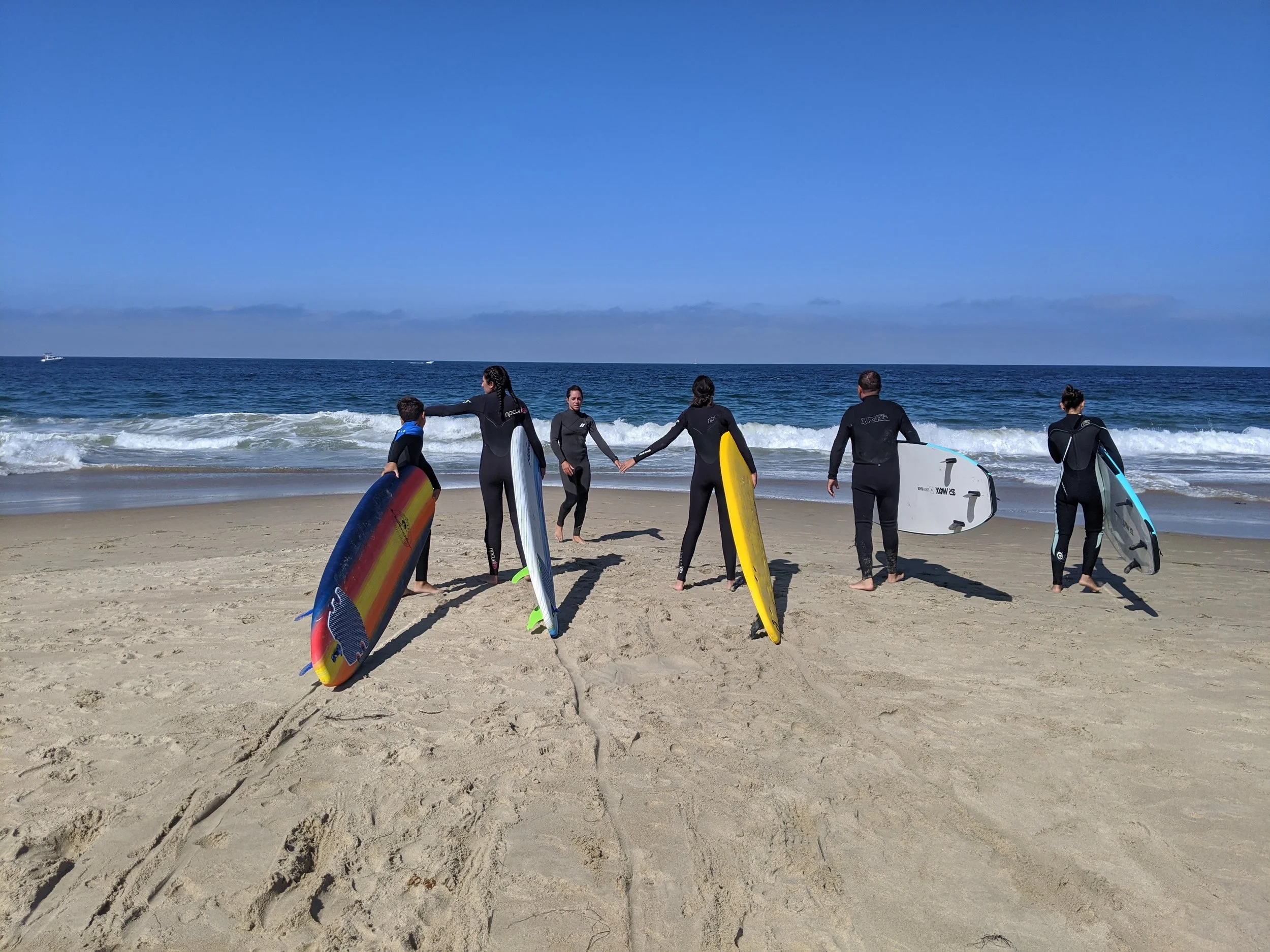 Surf lesson group walking hand in hand toward the waves with colorful boards