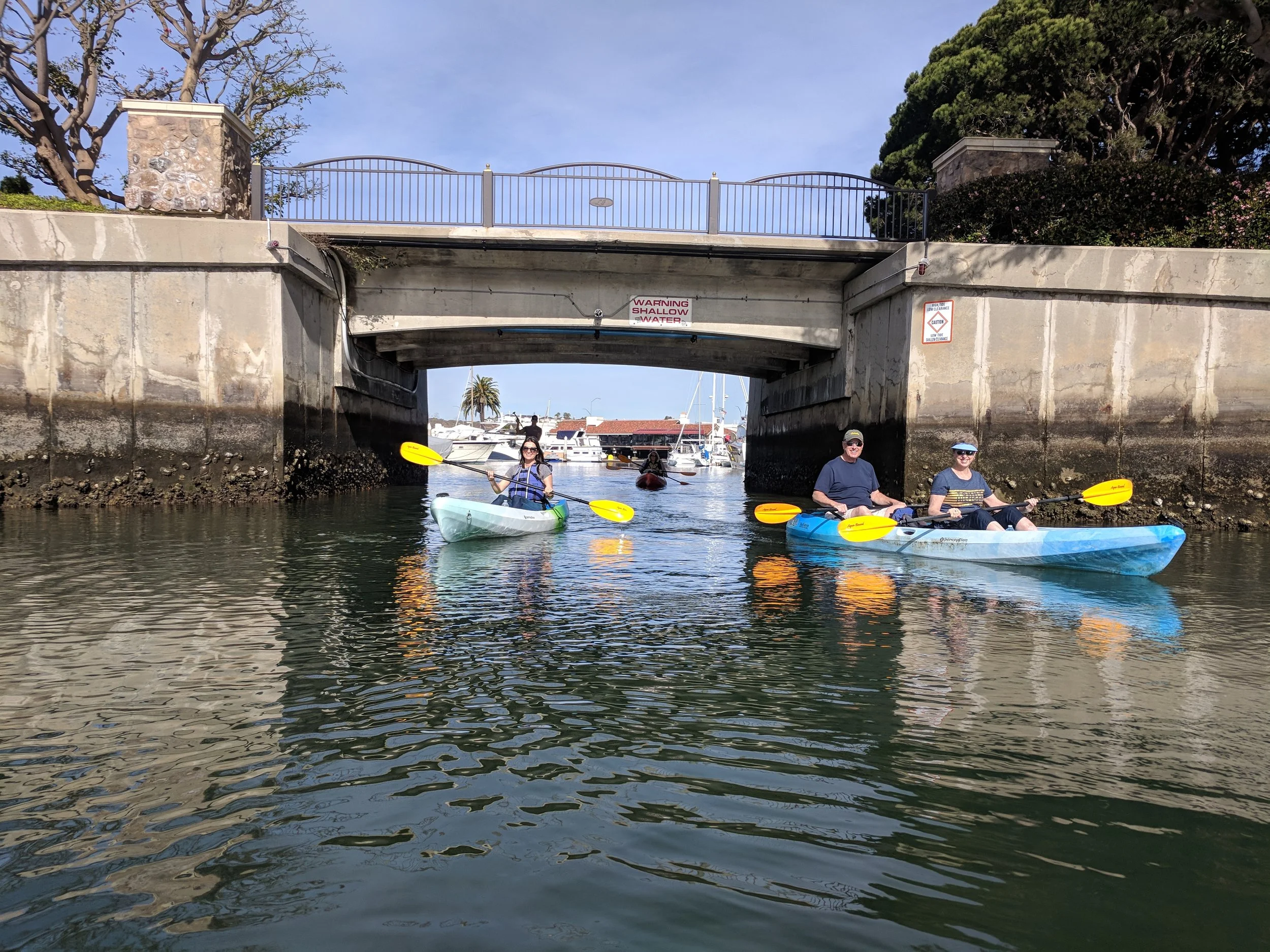 Team kayaking under a bridge in the Newport Beach channels