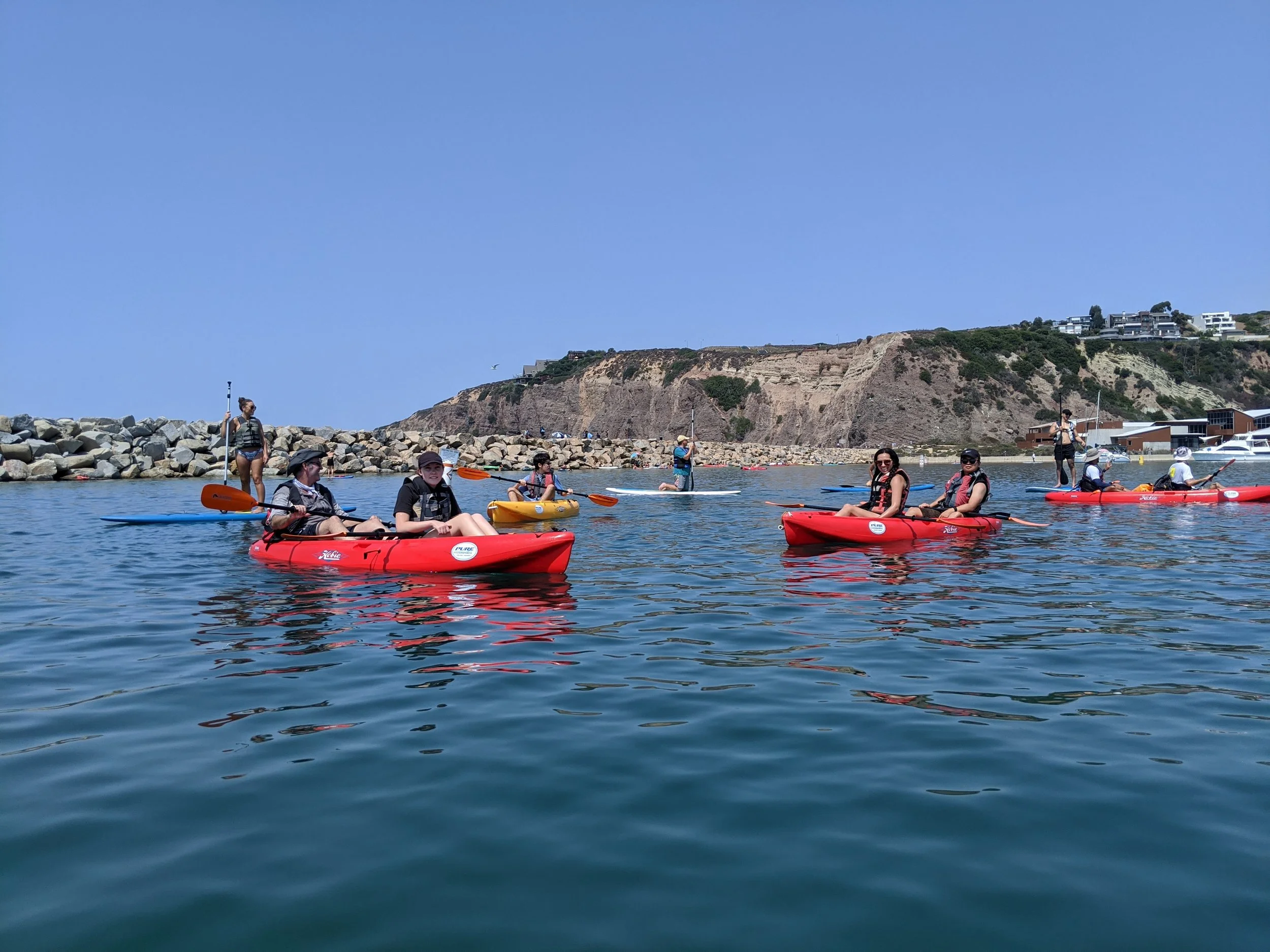 Red kayaks paddling beneath the Dana Point headlands
